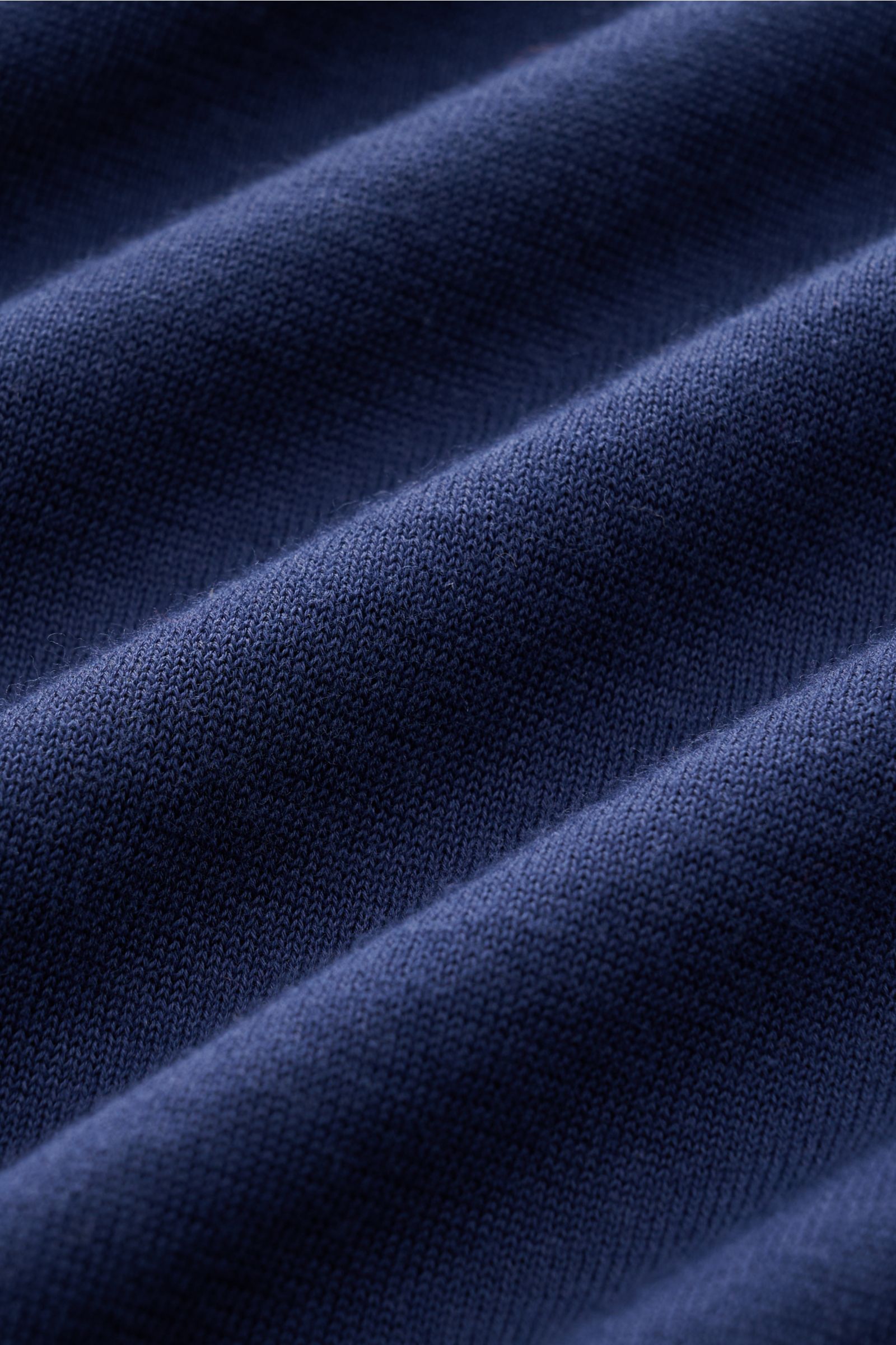 Nahaufnahme des feinen Strickbilds eines navyfarbenen Drumohr Kurzarm-Strickpolos aus weicher, atmungsaktiver Baumwolle, fotografiert in Detailperspektive.