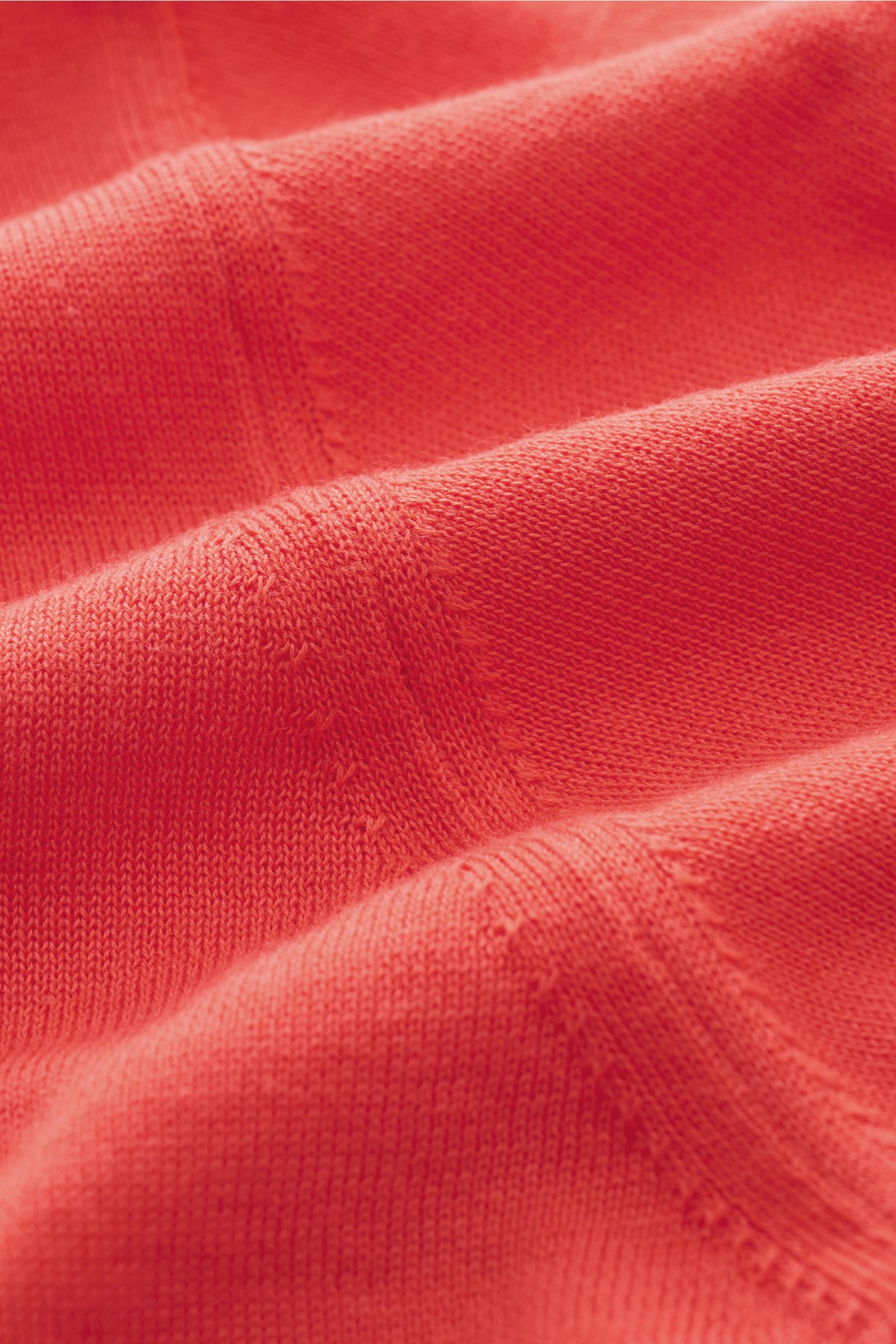 Nahaufnahme des roten Feinstrickstoffs, Detailansicht mit weichem Griff des Drumohr Kurzarm-Strickpolo rot aus reiner Baumwolle, fotografiert aus schräger Perspektive.