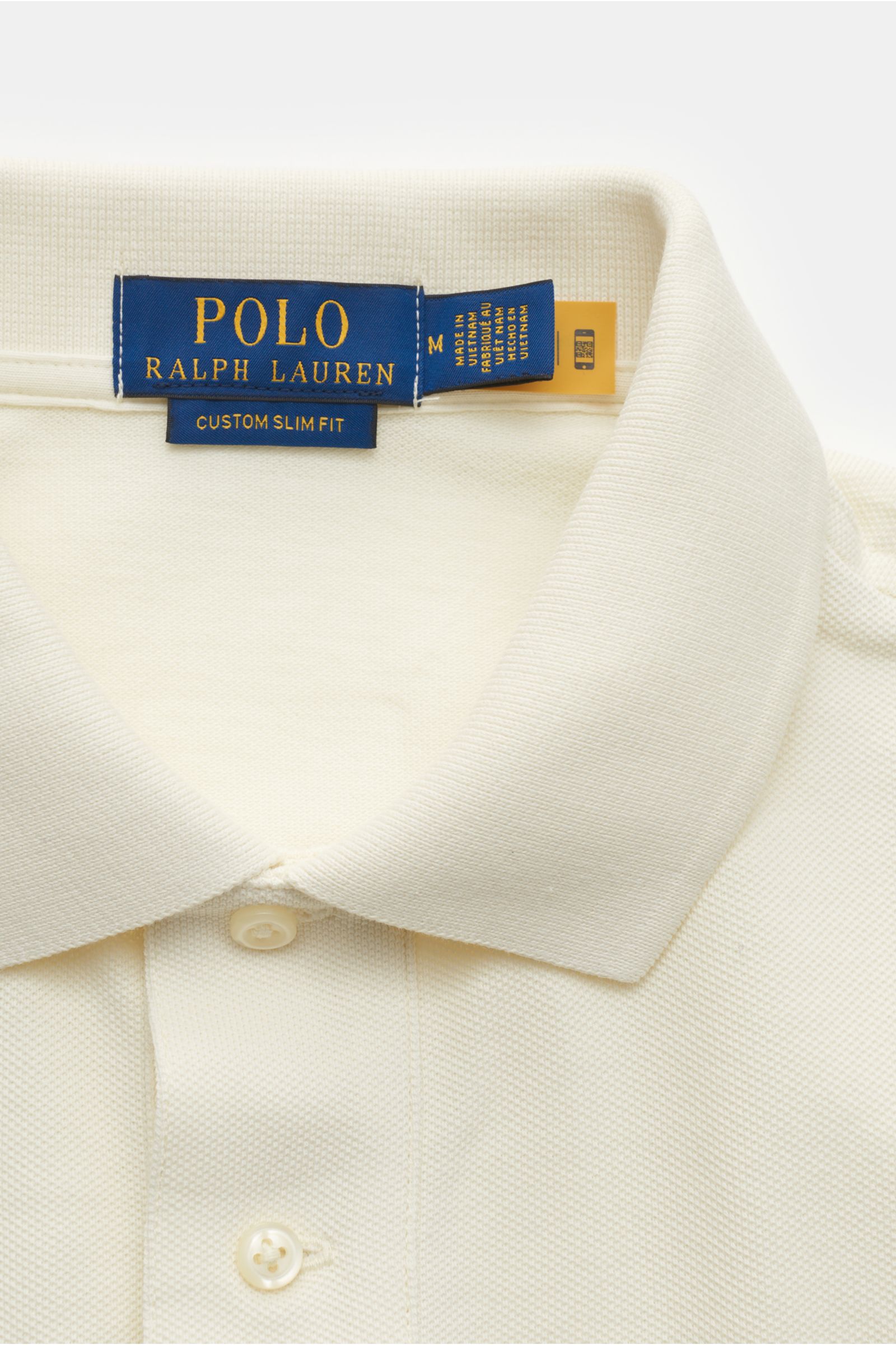 Nahaufnahme des cremefarbenen Polo Ralph Lauren Poloshirts aus reiner Baumwolle mit feiner Piqué-Struktur, Slim Fit, Polokragen und Zwei-Knopf-Leiste, fotografiert von oben.