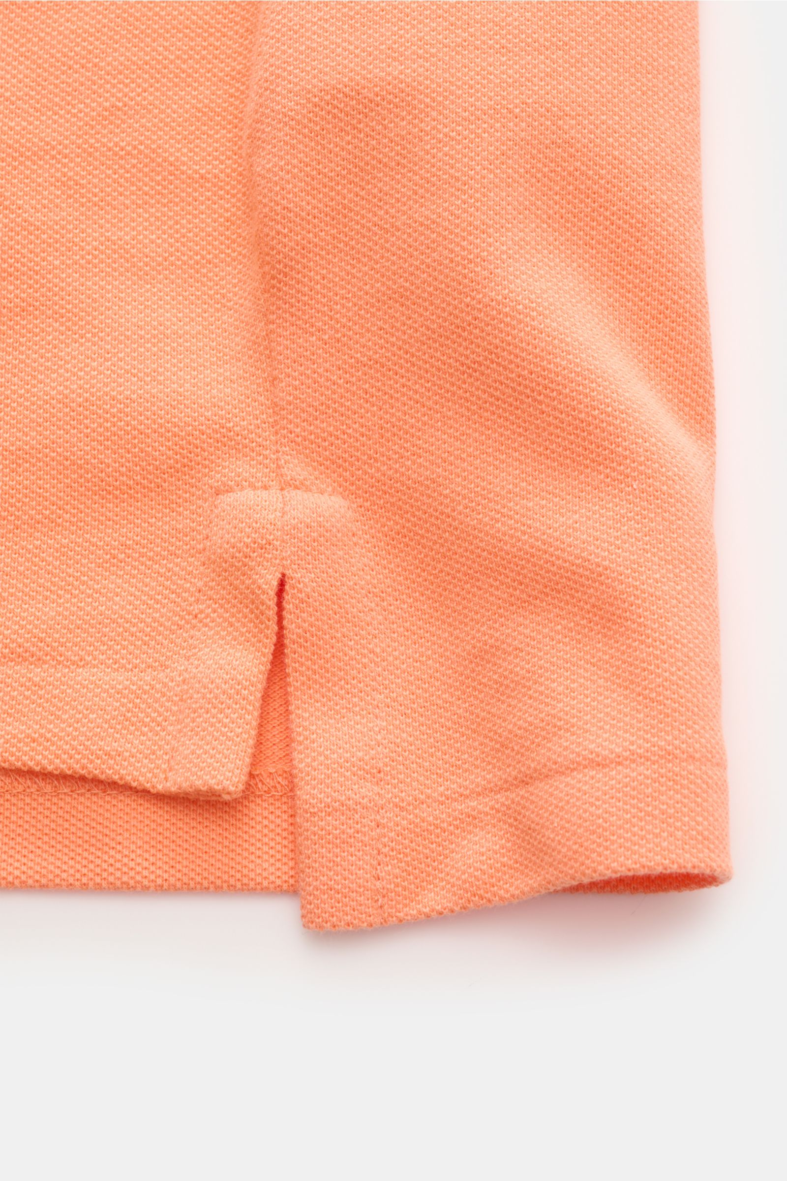 Close-up detail of the hem with side vents on the Polo Ralph Lauren Polo shirt orange, showcasing the fine piqué texture and lightweight cotton fabric from a side perspective. The classic among polo shirts since 1972: The iconic pure cotton piqué model wi
