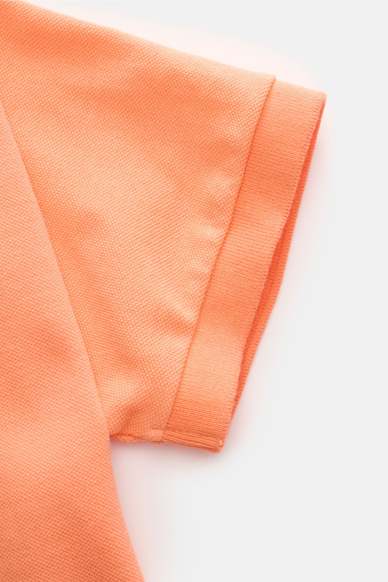 Close-up view of the sleeve of the Polo Ralph Lauren Polo shirt orange, showcasing the fine piqué texture and elasticated cuff. The classic among polo shirts since 1972: The iconic pure cotton piqué model with the famous polo rider stitching on the che