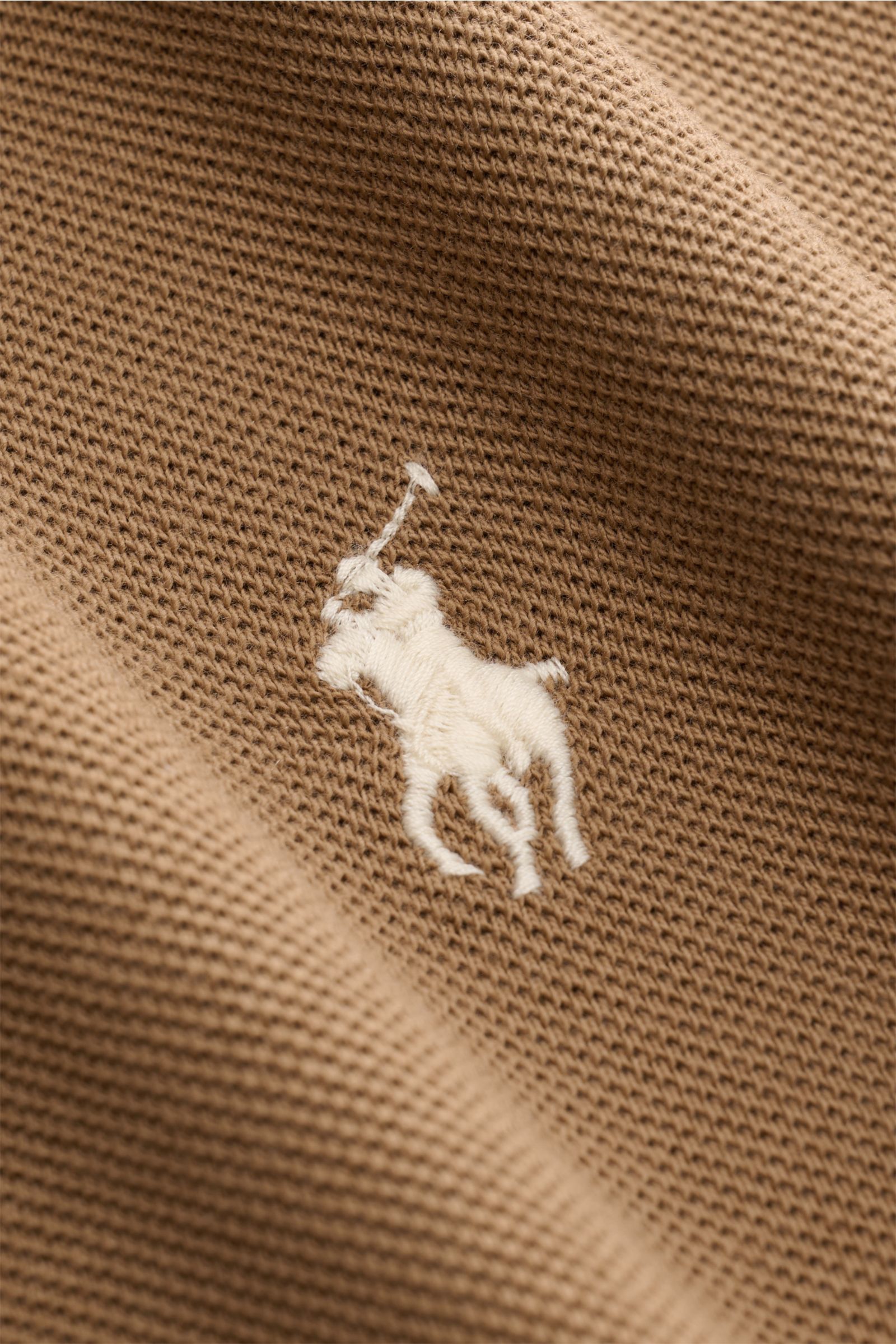 Polo Ralph Lauren Poloshirt braun, Nahaufnahme von der feinen Piqué-Struktur und dem weißen Poloreiter-Stitching auf Brusthöhe, reine Baumwolle.