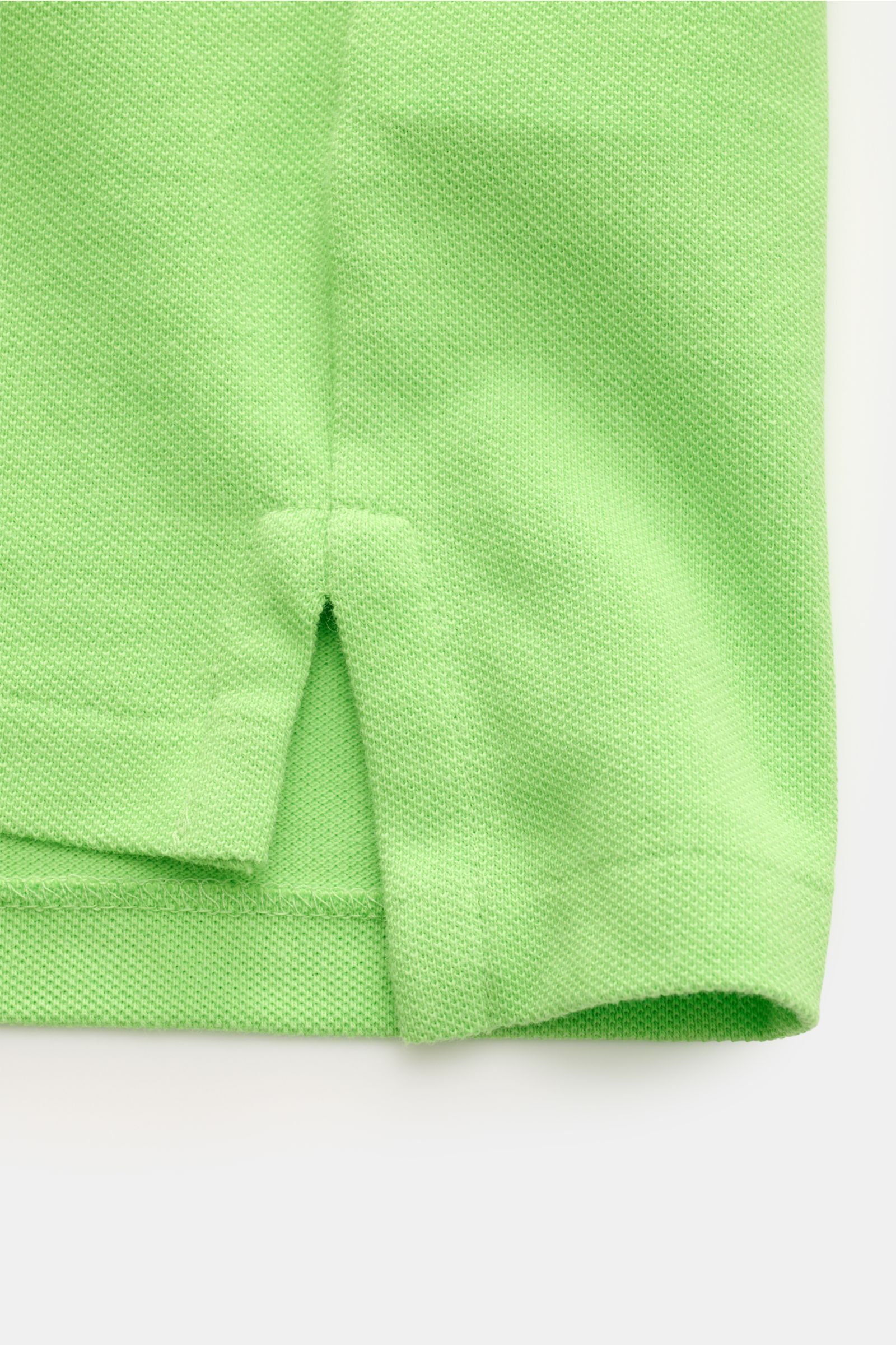Nahaufnahme der seitlichen Saumschlitze eines Polo Ralph Lauren Poloshirts neongrün aus reiner Baumwolle mit Piqué-Struktur und elastischen Bündchen.