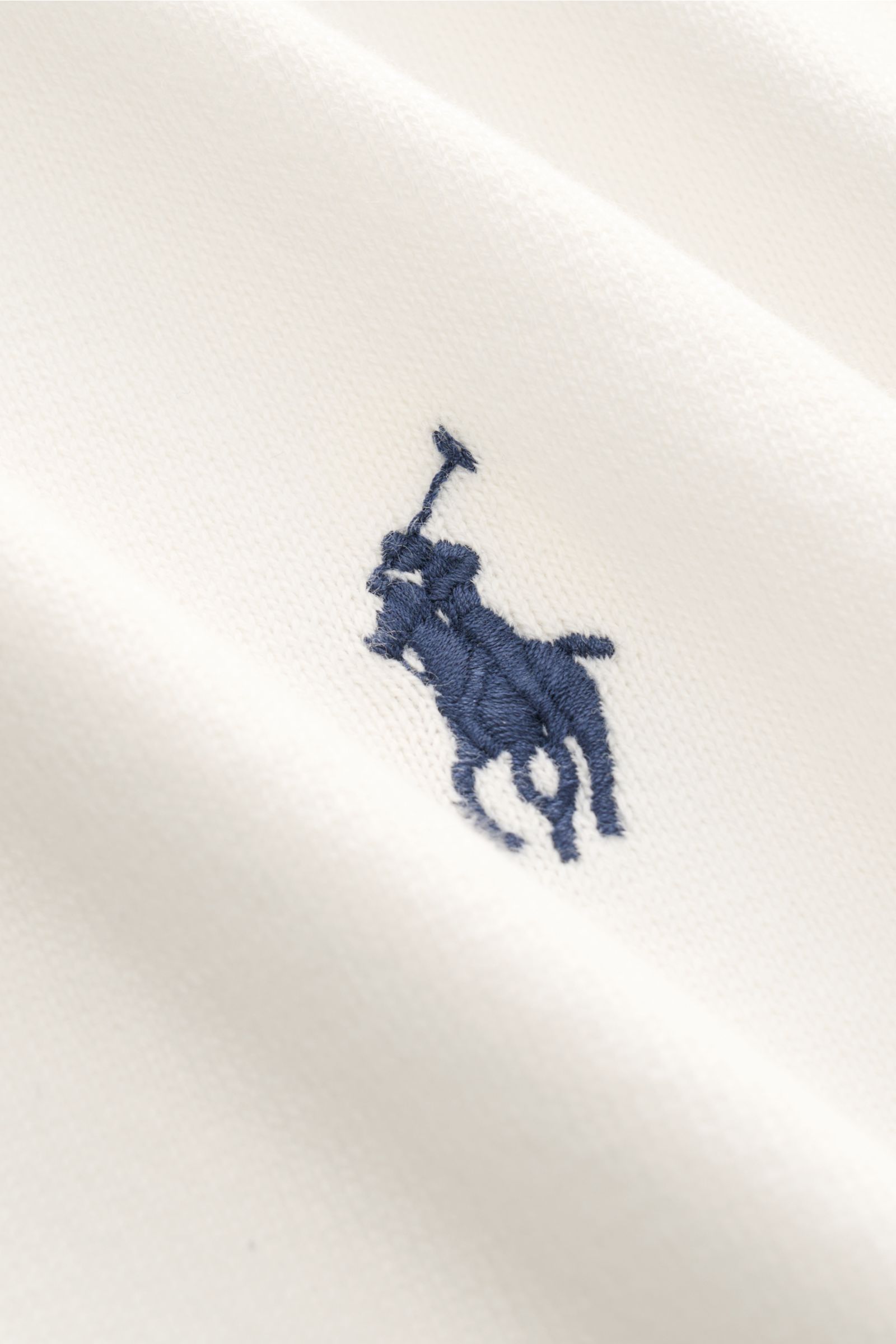 Close-up front view of Polo Ralph Lauren Kurzarm-Strickpolo offwhite showing fine cotton knit and navy logo stitching.

Description:  
Sommerlicher Klassiker: Das Kurzarm-Strickpolo von POLO RALPH LAUREN verbindet zeitloses Design mit höchstem Tragekom