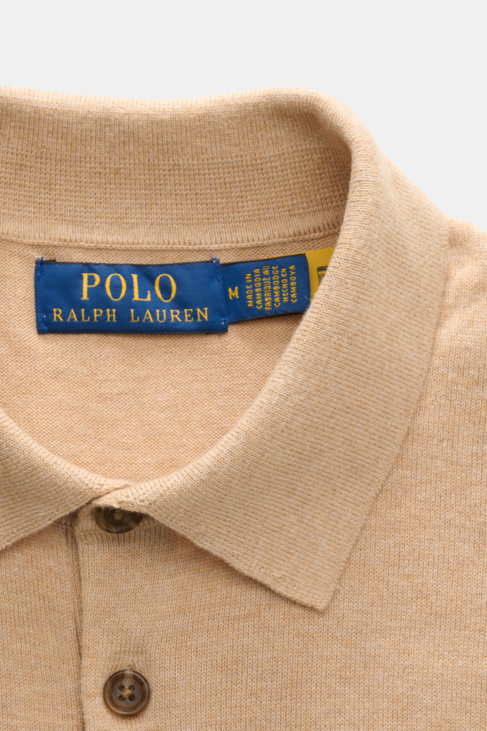 Close-up view of the collar and buttons of the Polo Ralph Lauren Kurzarm-Strickpolo beige meliert, showing fine knit texture and label.

Sommerlicher Klassiker: Das Kurzarm-Strickpolo von POLO RALPH LAUREN verbindet zeitloses Design mit höchstem Tragek