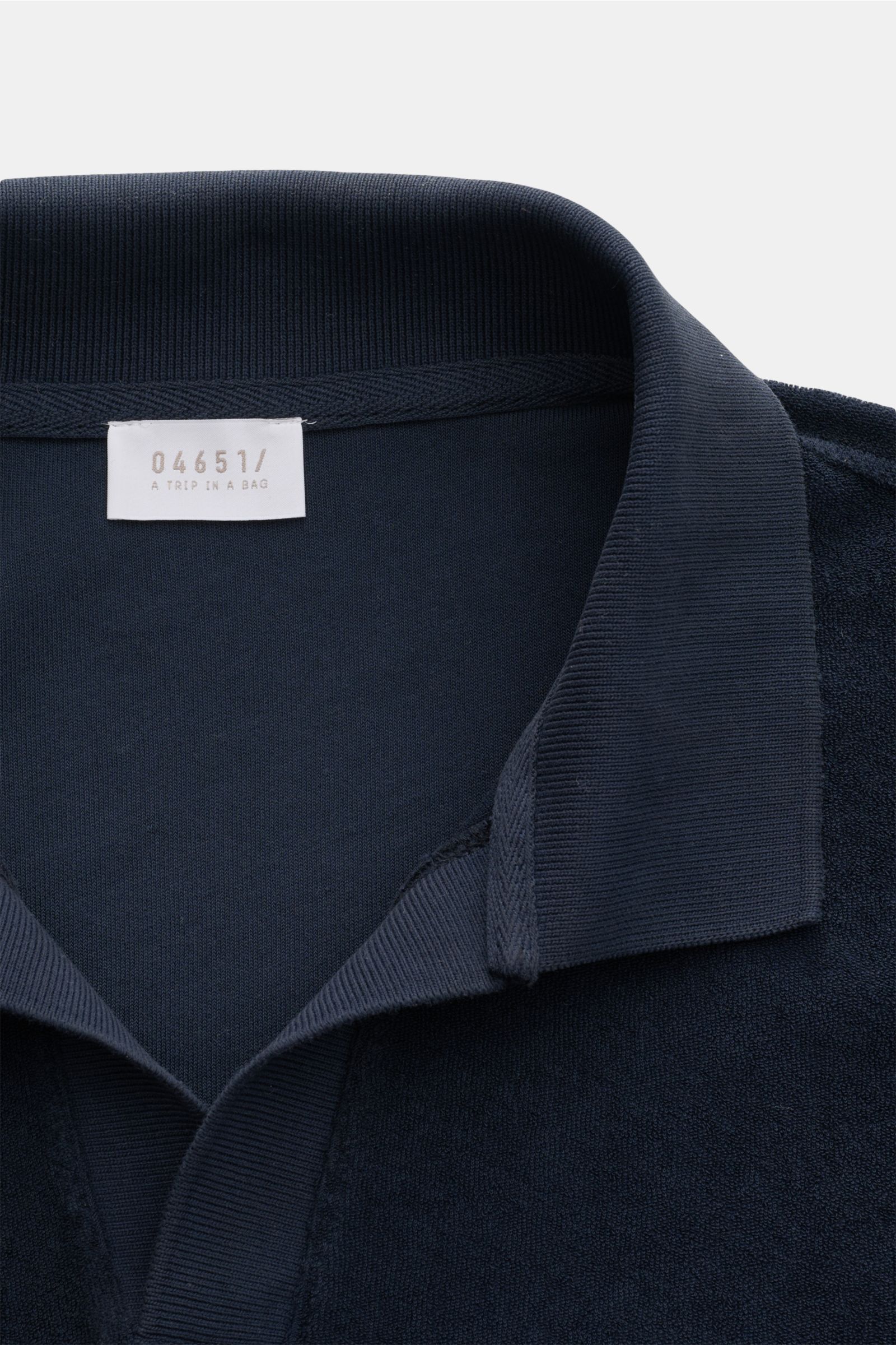 Nahaufnahme des navyfarbenen 04651/ A trip in a bag Frottee-Poloshirt 'Terry Johnny' mit offenem Polokragen aus Baumwoll-Frottee, weicher Griff, Regular Fit, Weblabel an der Seitennaht, kurze Saumschlitze, fotografiert von oben. Urlaubsgefühl zum Anziehen