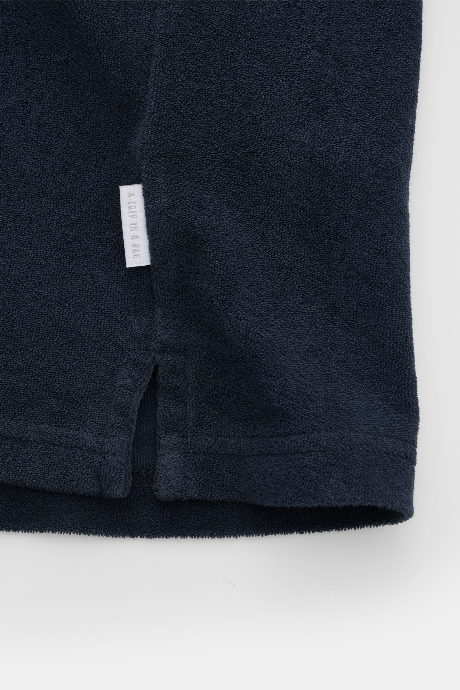 Nahaufnahme des Saumabschnitts mit kurzen Saumschlitzen und kleinem Weblabel der Seitennaht am 04651/ A trip in a bag Frottee-Poloshirt 'Terry Johnny' navy aus weichem Baumwoll-Frottee.