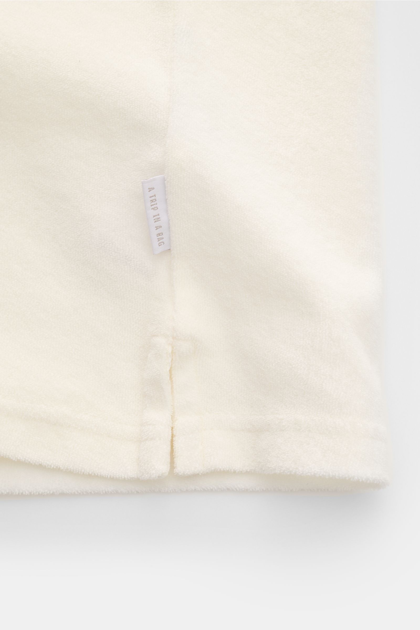 04651/ A trip in a bag Frottee-Poloshirt 'Terry Johnny' offwhite, Detailansicht von Saum mit kurzem Schlitz und Weblabel aus Baumwoll-Frottee.