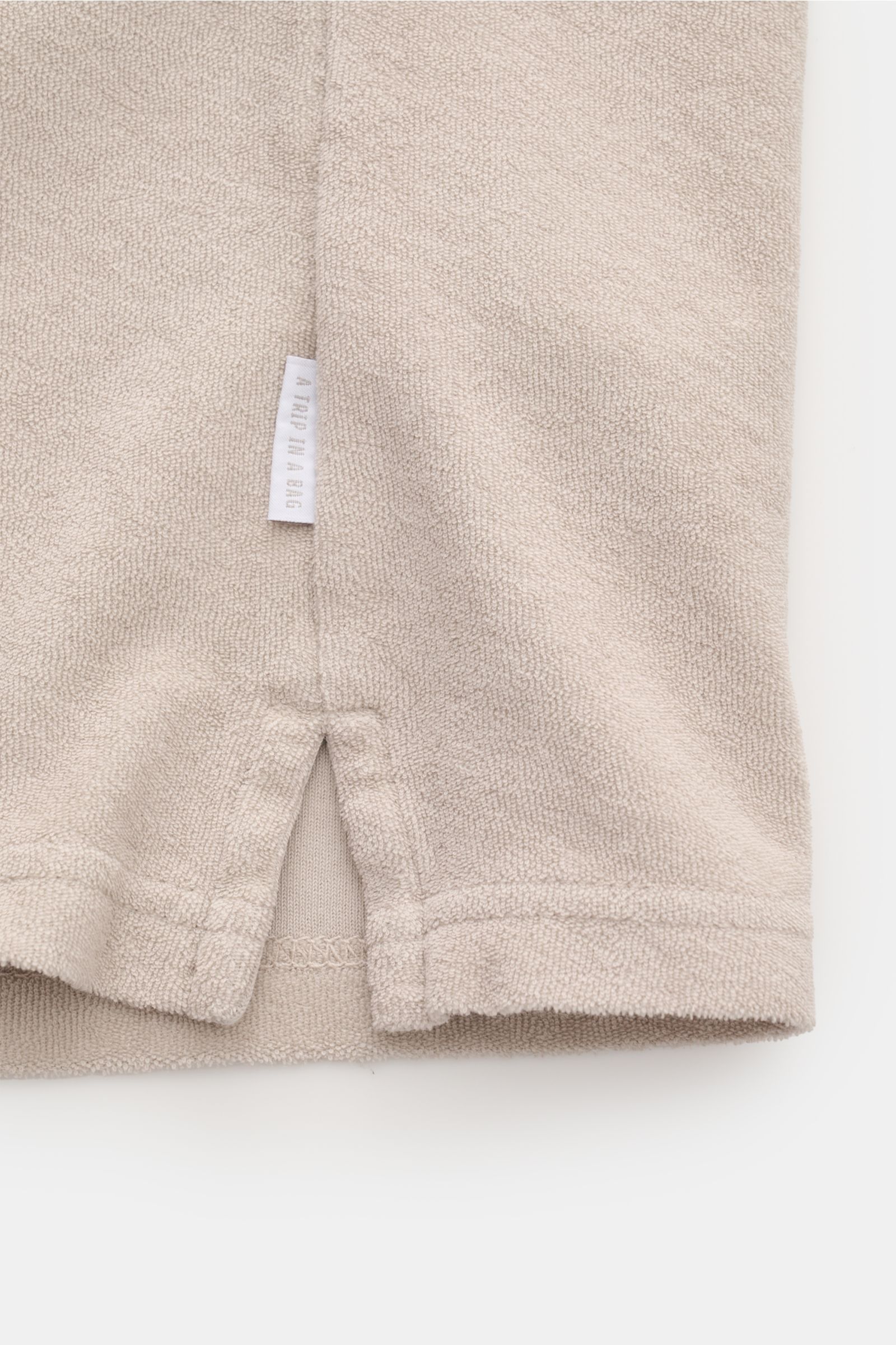 Close-up from the bottom side of the beige 04651/ A trip in a bag Terry polo shirt 'Terry Johnny' showing terrycloth texture, small woven label, and short hem vents.

Description: Holiday feel you can wear: This short sleeve polo shirt in comfortable c