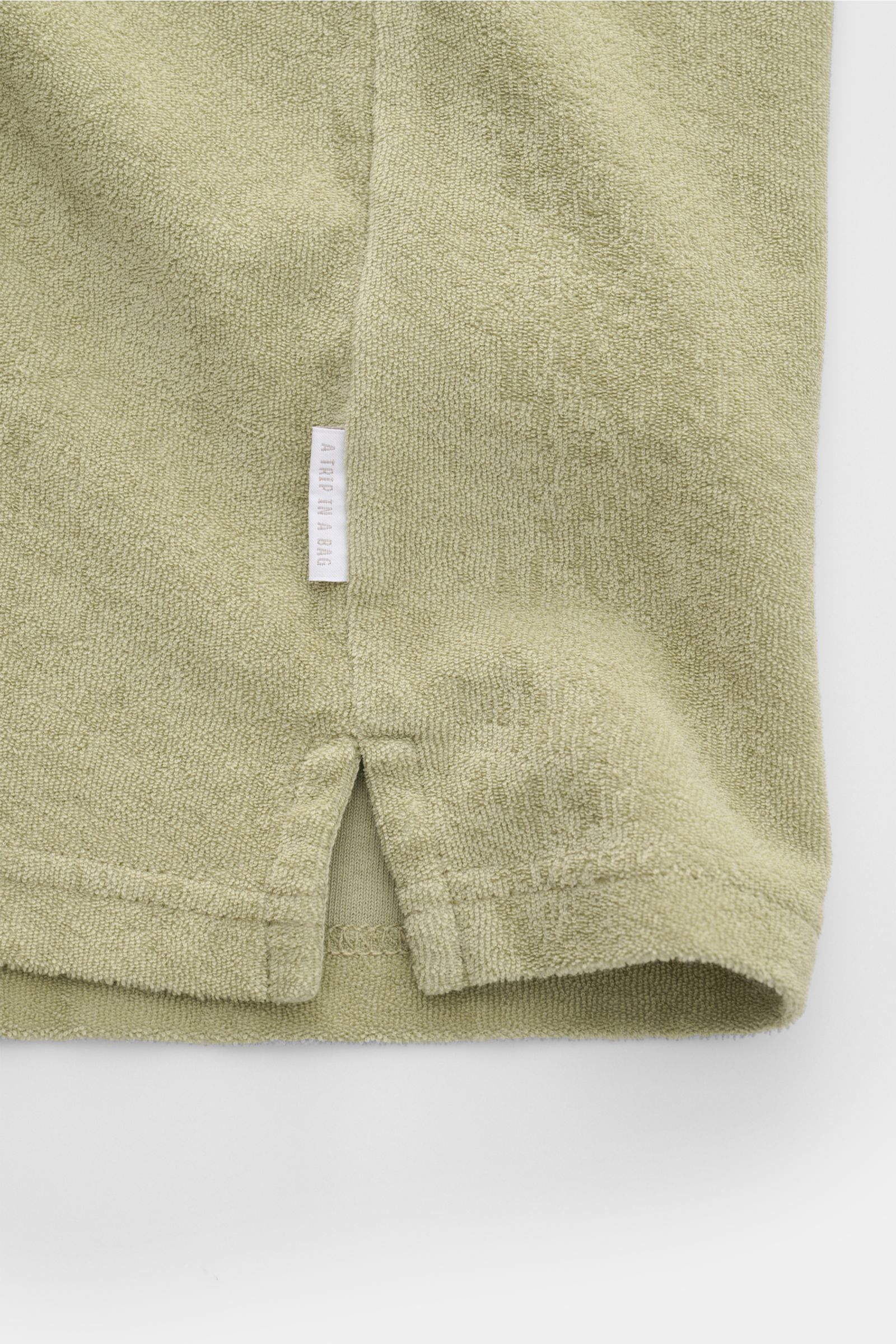04651/ A trip in a bag Frottee-Poloshirt 'Terry Johnny' salbei, Detailaufnahme Saum mit kurzen Schlitzen und kleinem Weblabel aus Baumwoll-Frottee.