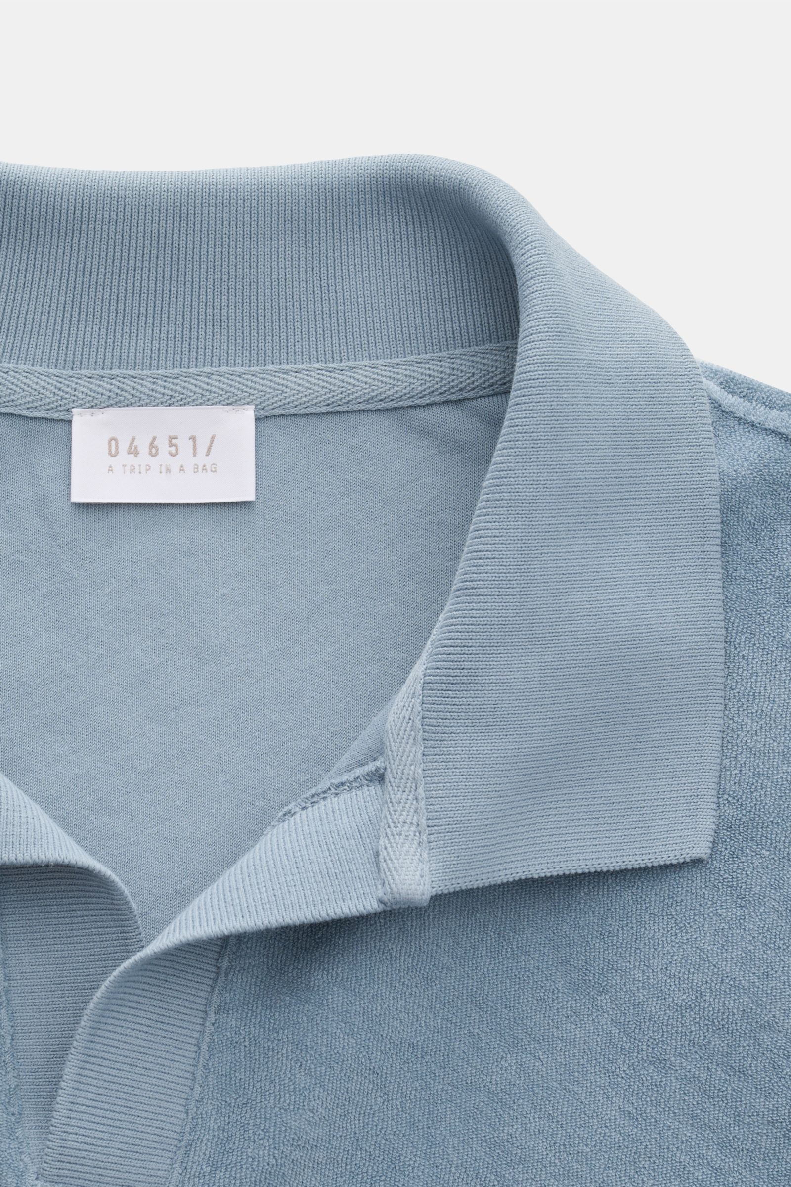 Close-up front view of the 04651/ A trip in a bag Terry polo shirt 'Terry Johnny' smoky blue showing the collar and label. Holiday feel you can wear: This short sleeve polo shirt in comfortable cotton terry by 04651/ A TRIP IN A BAG is a casual and comfor
