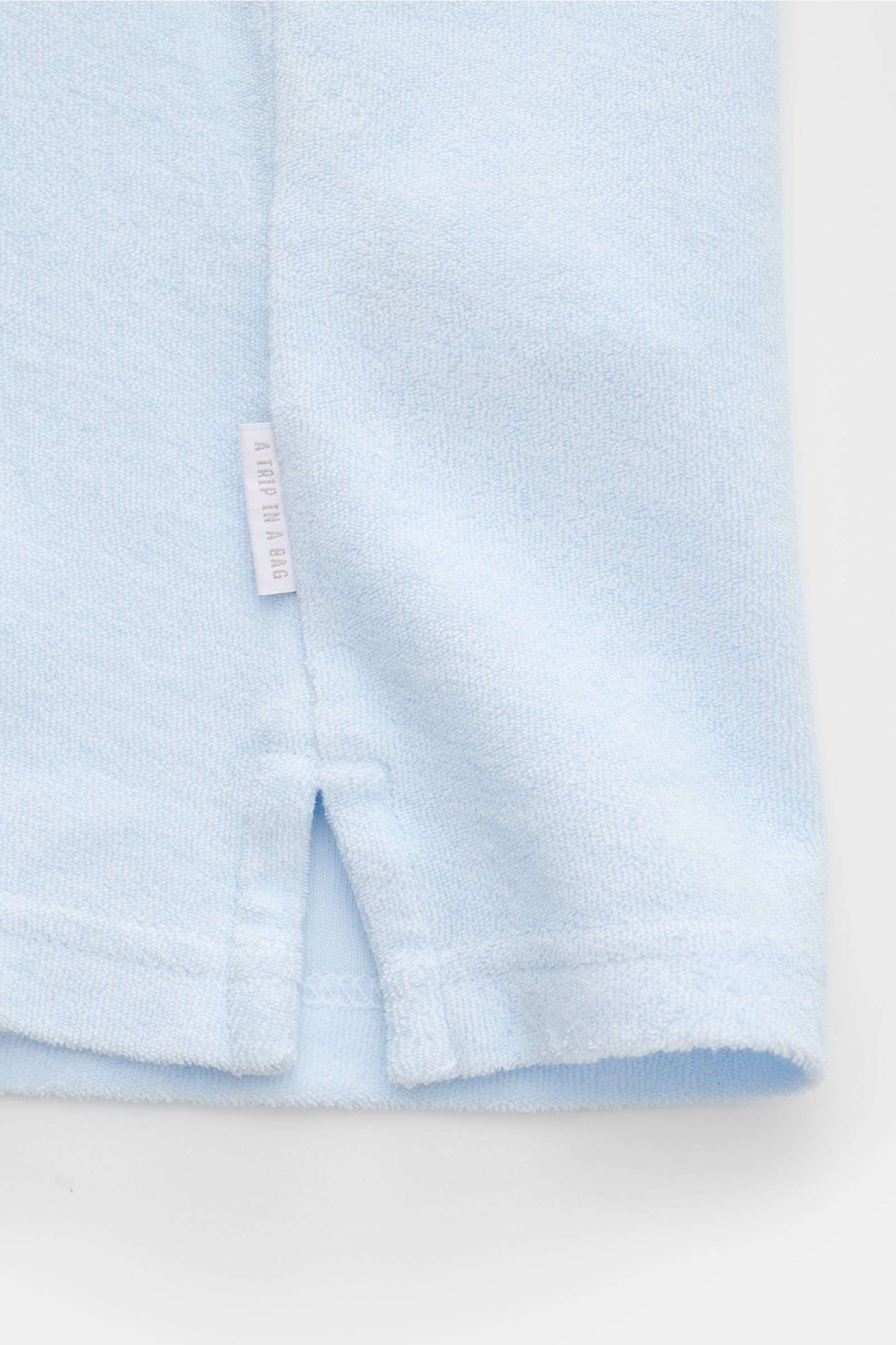 Close-up front view of the hem and side seam of the 04651/ A trip in a bag Terry polo shirt 'Terry Johnny' pastel blue, showing the small woven label and short hem vents in soft cotton terrycloth.

Holiday feel you can wear: This short sleeve polo shir