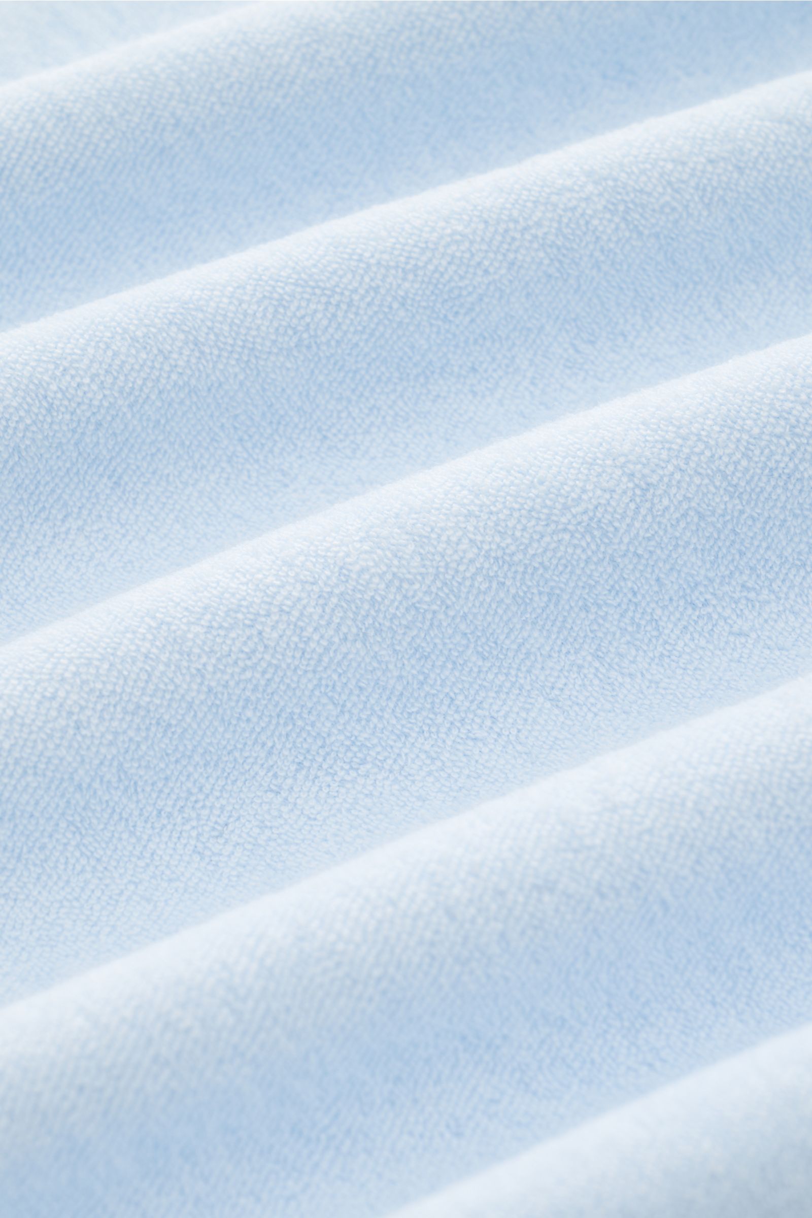 Close-up front view of the pastel blue 04651/ A trip in a bag Terry polo shirt 'Terry Johnny' showing soft cotton terry texture with signature collar and short hem vents. Holiday feel you can wear: This short sleeve polo shirt in comfortable cotton terry 