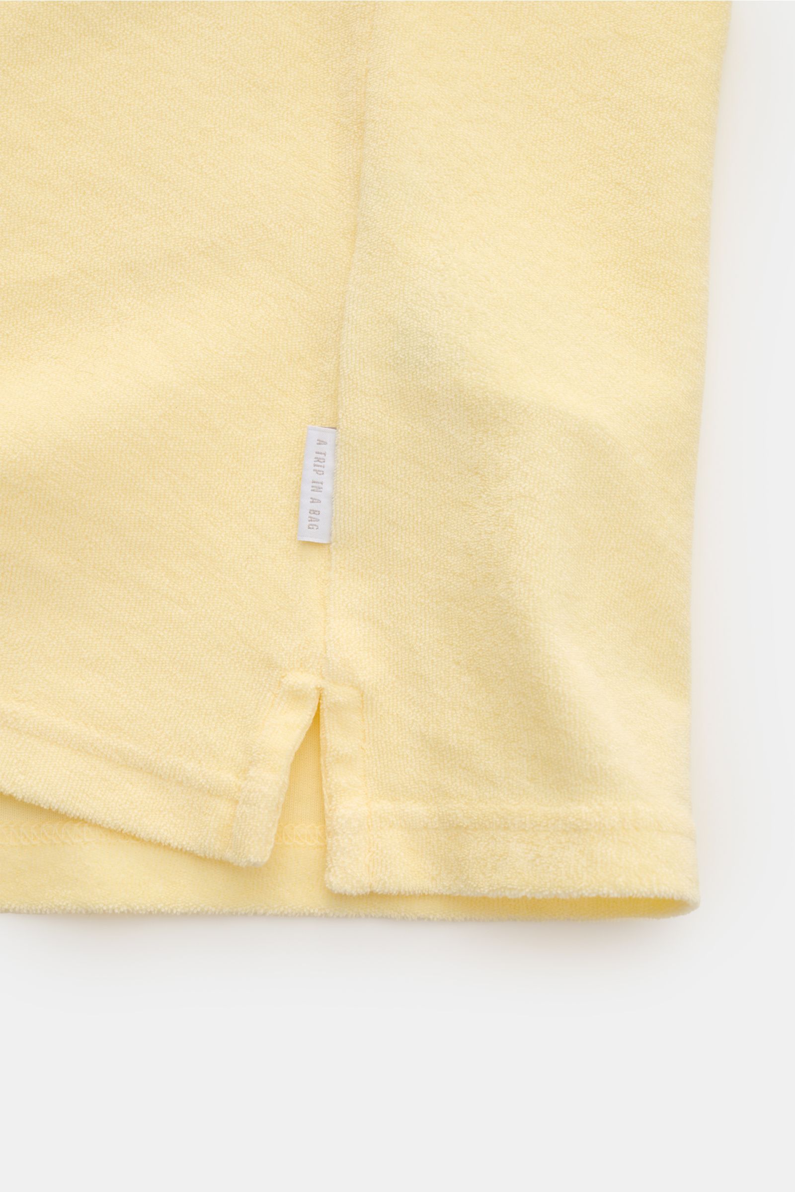 Close-up front view of the hem detail on the 04651/ A trip in a bag Terry polo shirt 'Terry Johnny' pastel yellow, showing the short hem vents and small woven label.

Holiday feel you can wear: This short sleeve polo shirt in comfortable cotton terry b