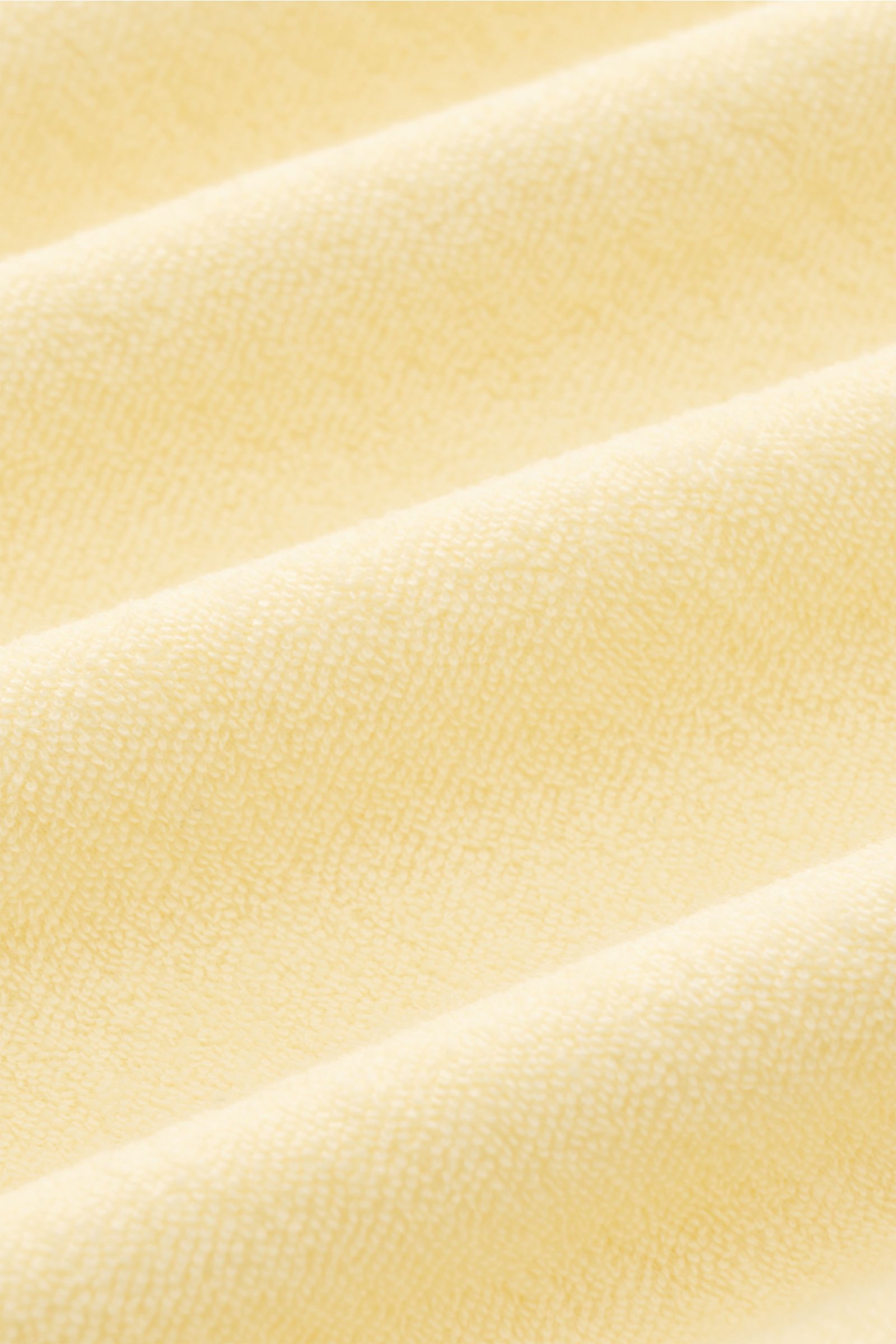 Close-up front view of 04651/ A trip in a bag Terry polo shirt 'Terry Johnny' pastel yellow fabric texture. Holiday feel you can wear: This short sleeve polo shirt in comfortable cotton terry by 04651/ A TRIP IN A BAG is a casual and comfortable essential