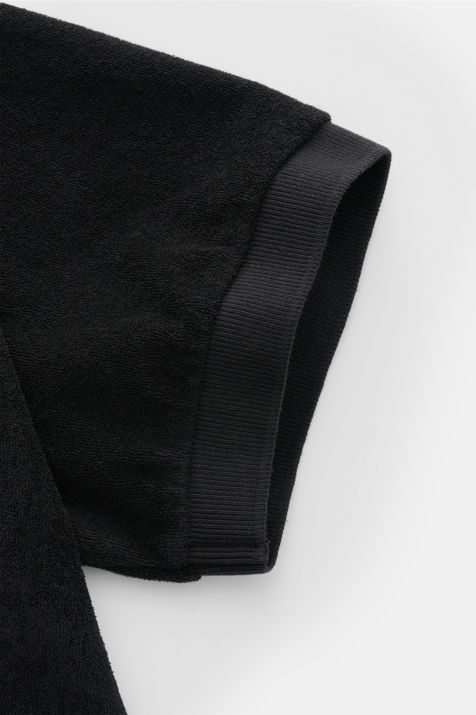 Schwarzer Ärmel des 04651/ A trip in a bag Frottee-Poloshirt 'Terry Johnny' in Nahaufnahme, weicher Baumwoll-Frottee, kurzer Saum, seitliches Weblabel.