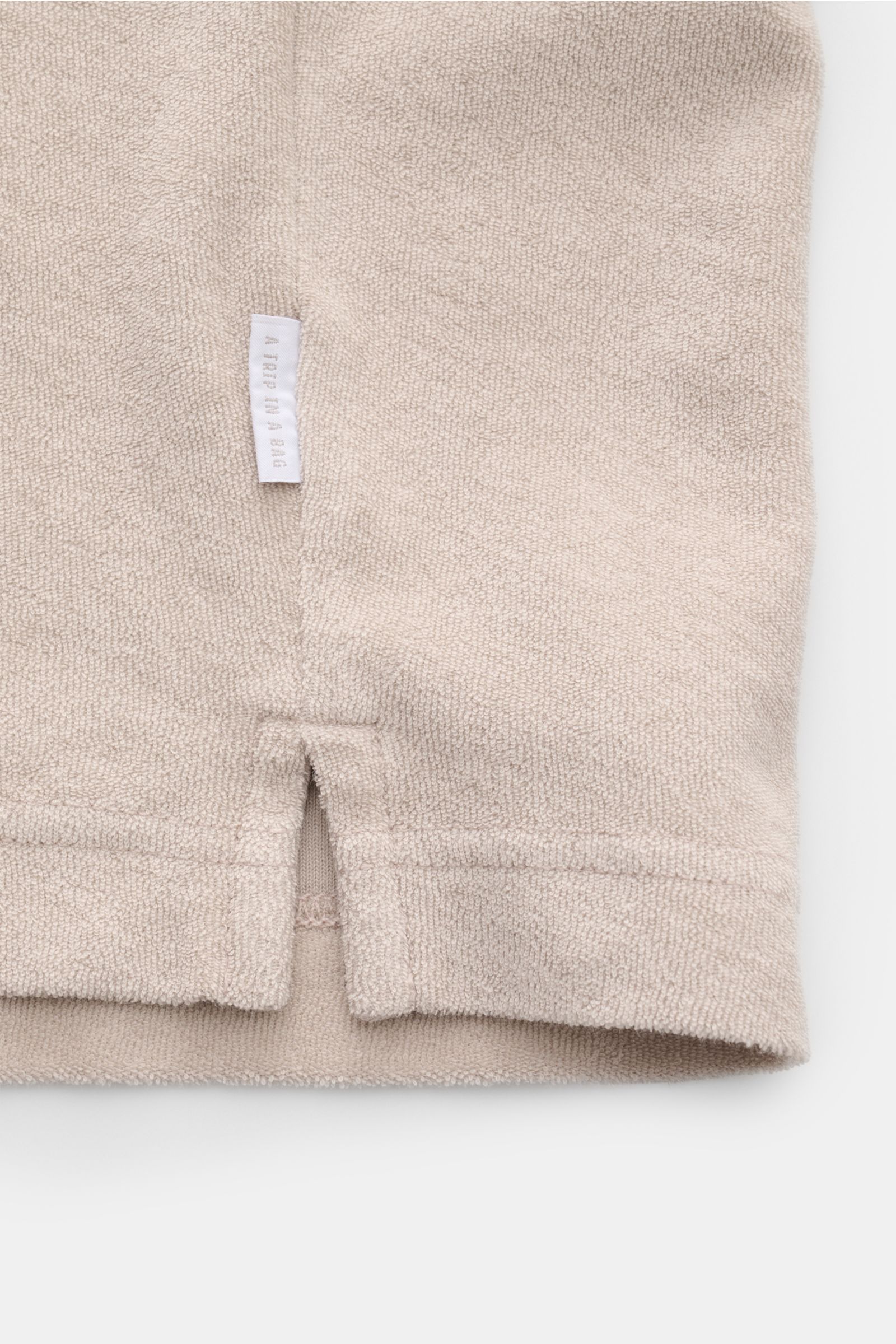 Beige Detailaufnahme des Saumabschlusses mit kurzem Schlitz und kleinem Weblabel des 04651/ A trip in a bag Frottee-Poloshirt 'Terry Polo' aus reiner Baumwolle.