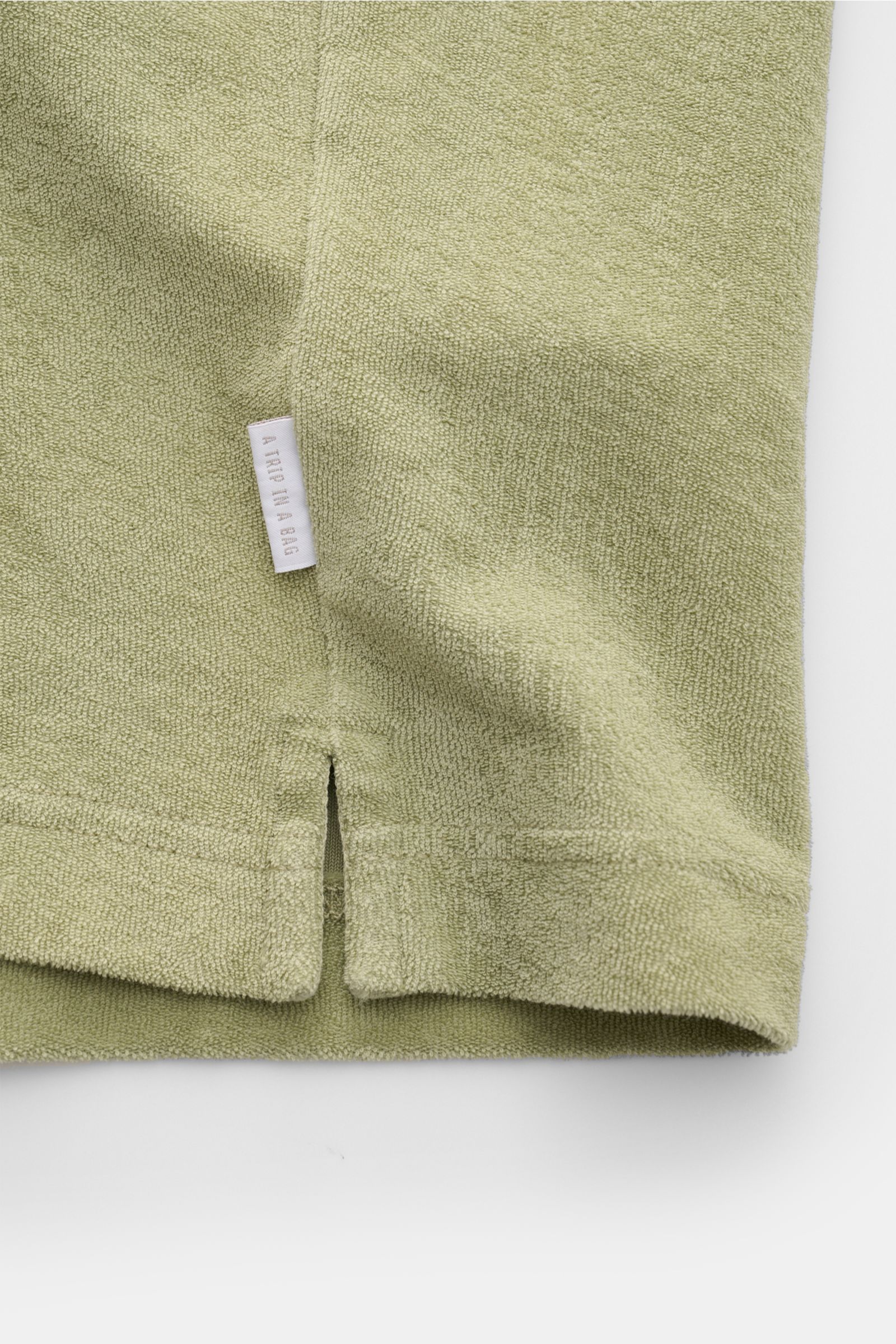 04651/ A trip in a bag Frottee-Poloshirt 'Terry Polo' salbei, Detailaufnahme des kurzen Saums mit Schlitzen und kleinem Weblabel aus reiner Baumwolle.