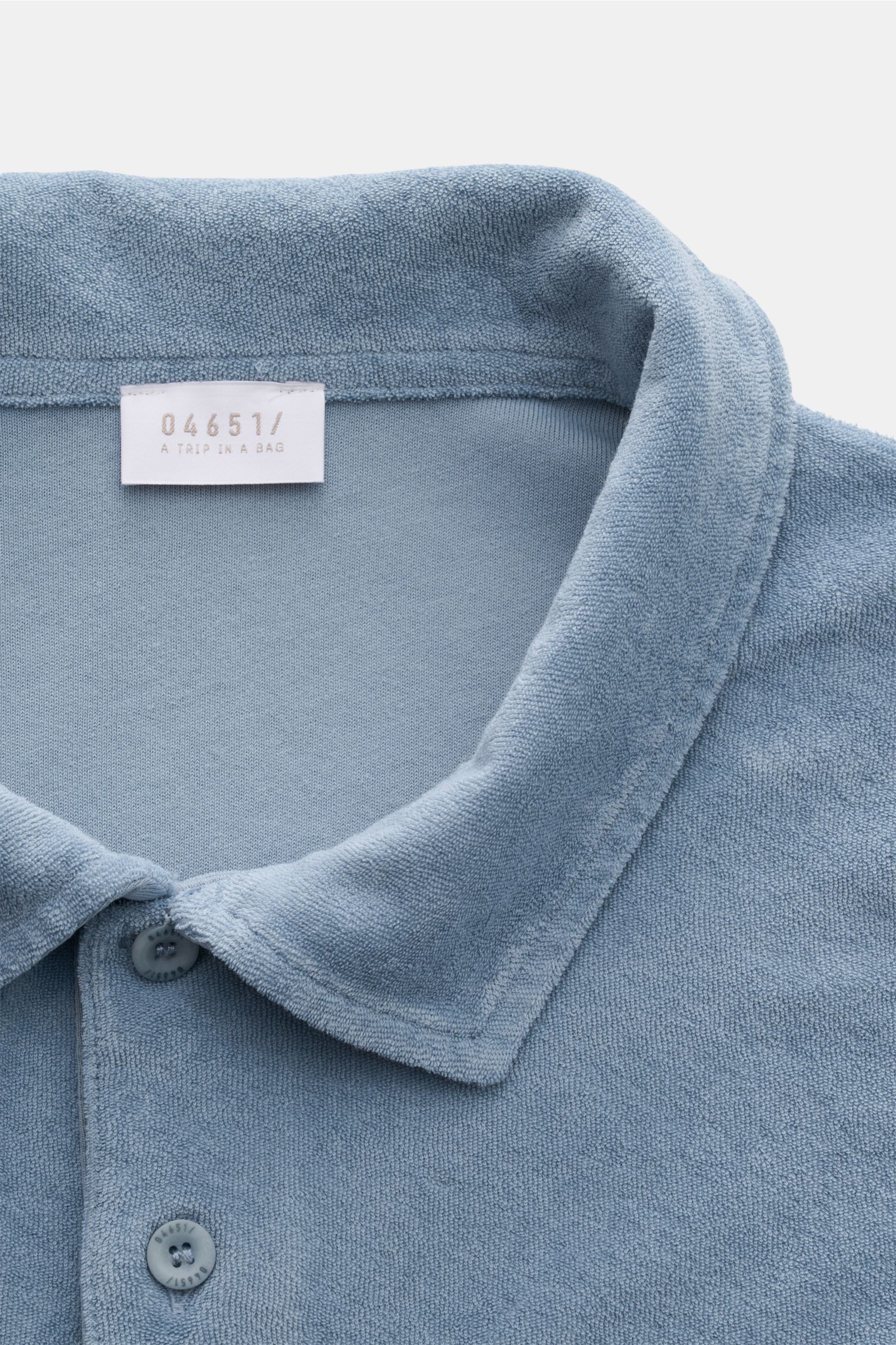 Nahaufnahme aus leicht schräger Perspektive des 04651/ A trip in a bag Frottee-Poloshirt 'Terry Polo' rauchblau aus reiner Baumwolle mit Polokragen, Knopfleiste und weichem Griff.