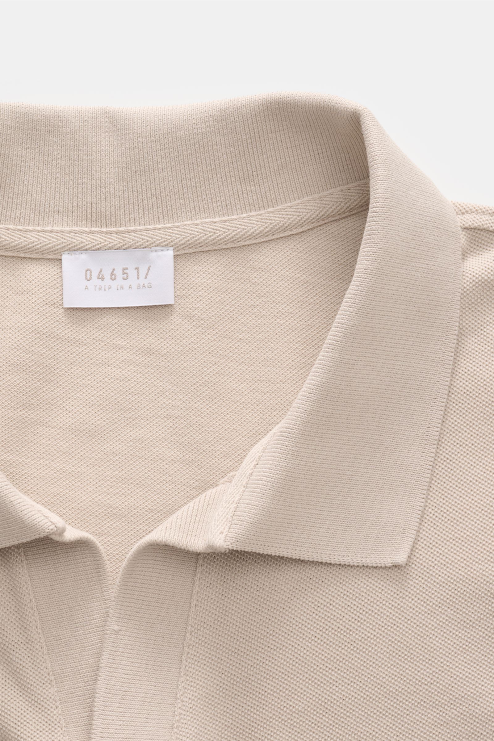 Nahaufnahme des beigefarbenen 04651/ A trip in a bag Poloshirts 'Johnny' aus reiner Baumwolle mit offenem Kragen, Piqué-Struktur und kleinem Weblabel.
