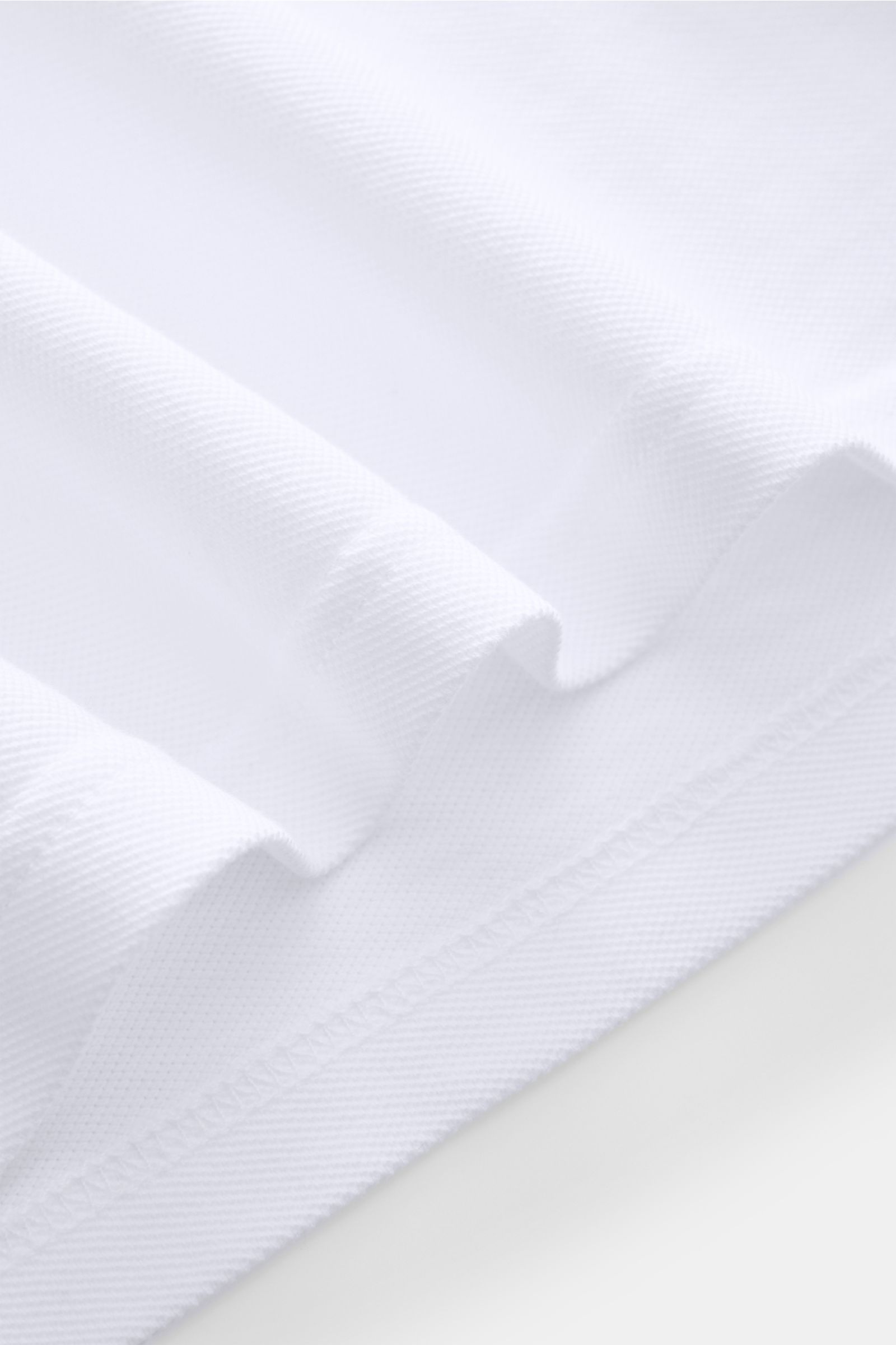 04651/ A trip in a bag Poloshirt 'Johnny' weiß, Nahaufnahme des weißen Baumwoll-Piqués mit offenem Kragen, Regular Fit, Saumschlitzen und Ärmelbündchen aus seitlicher Perspektive.