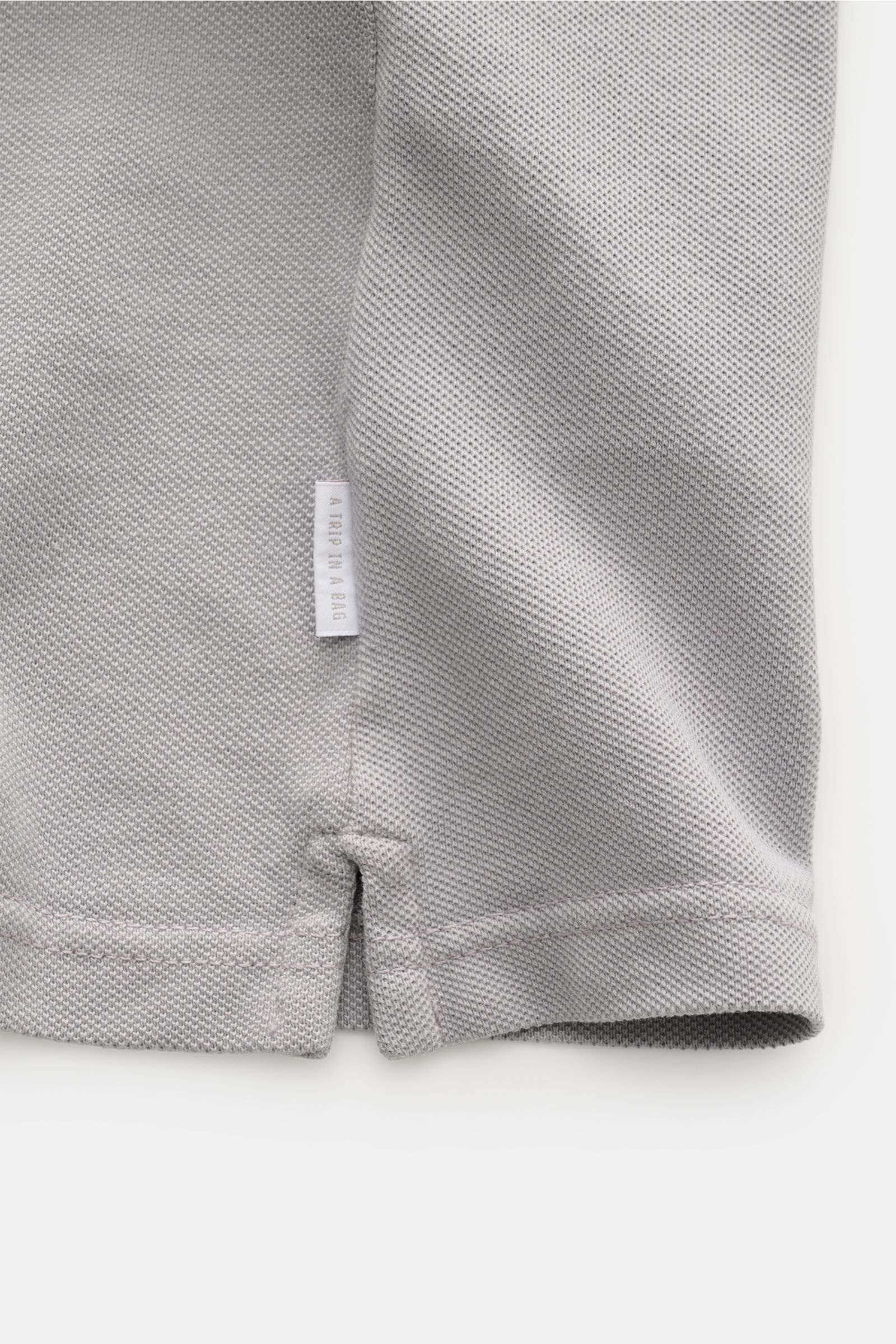 Close-up side hem view of 04651/ A trip in a bag Polo shirt 'Johnny' grey in pure piqué cotton with small woven label.

For relaxed casual looks: 04651/ A TRIP IN A BAG brings a relaxed summer vibe to your wardrobe with this pure cotton polo shirt feat