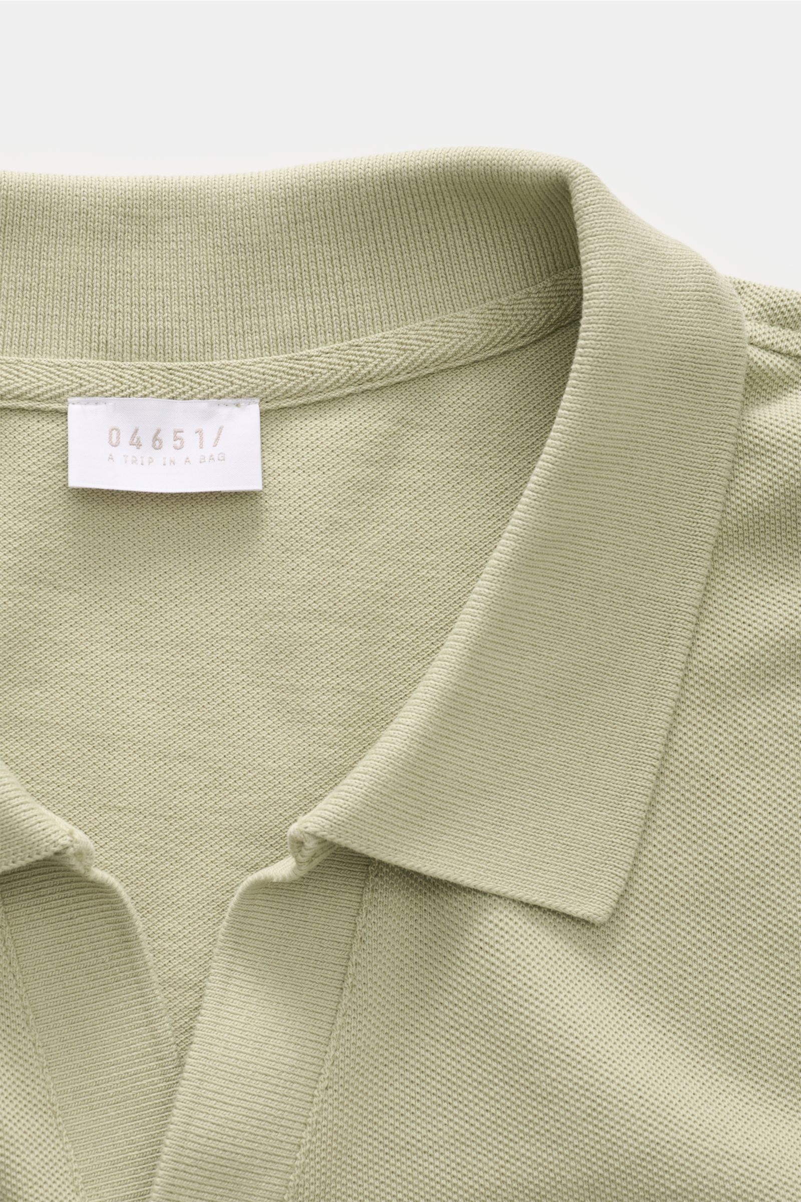 Nahaufnahme des salbeifarbenen 04651/ A trip in a bag Poloshirts 'Johnny' aus reiner Baumwolle mit offenem Kragen und Piqué-Struktur.