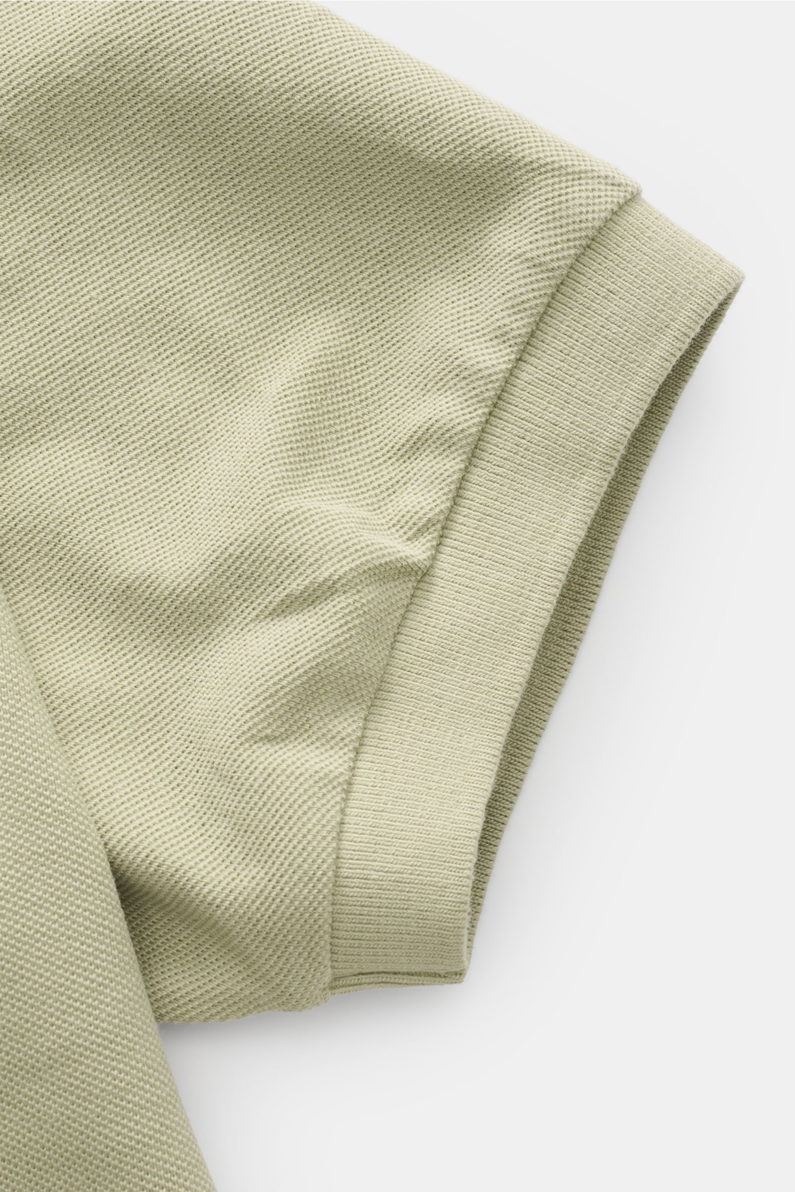 Nahaufnahme des Ärmels vom 04651/ A trip in a bag Poloshirt 'Johnny' salbei aus reiner Baumwolle mit offener Kragenleiste und kurzen Saumschlitzen.