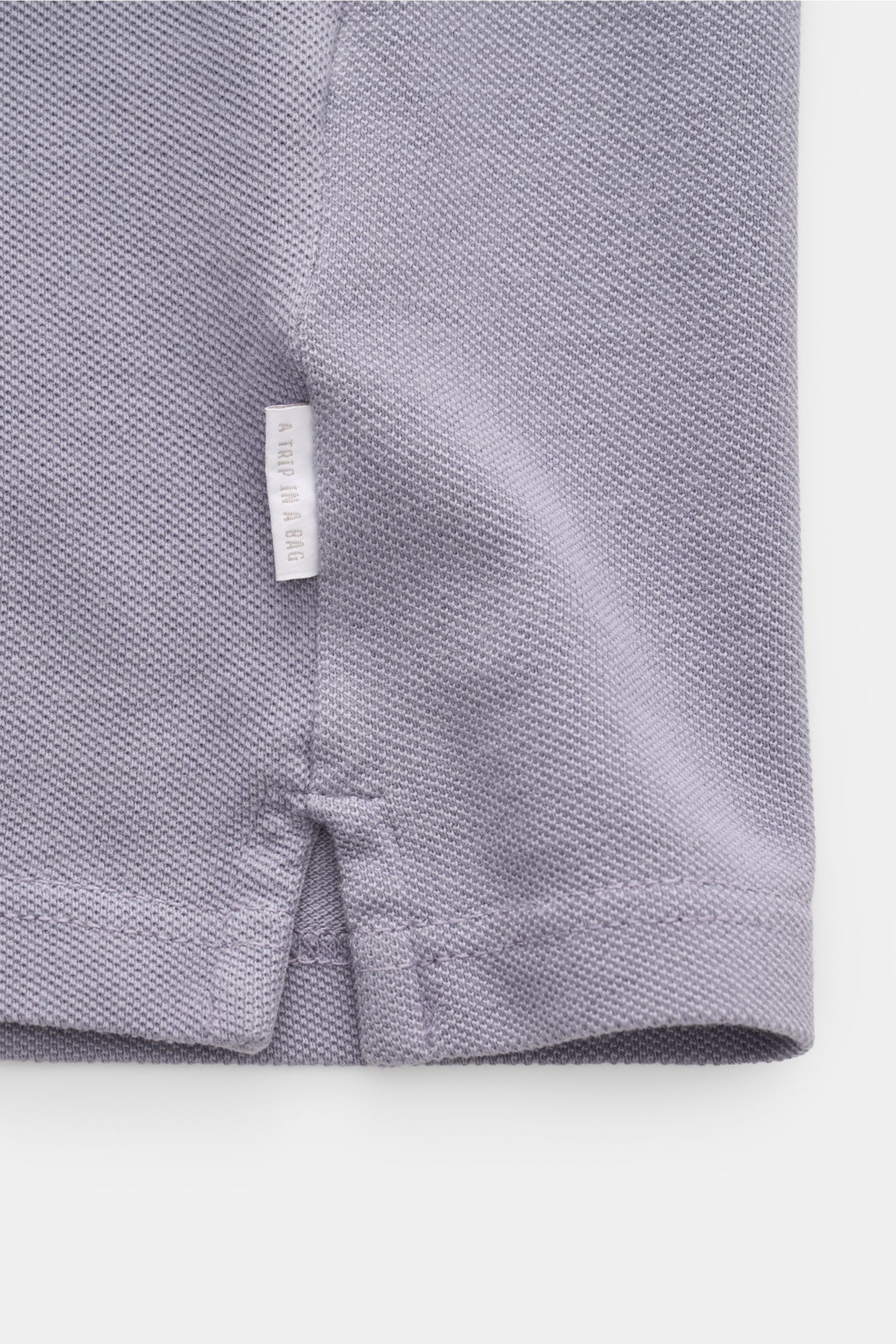 Nahaufnahme des Saumdetails eines 04651/ A trip in a bag Poloshirts 'Johnny' lavender aus reiner Baumwolle, Regular Fit mit offenem Kragen und kleinem Weblabel.