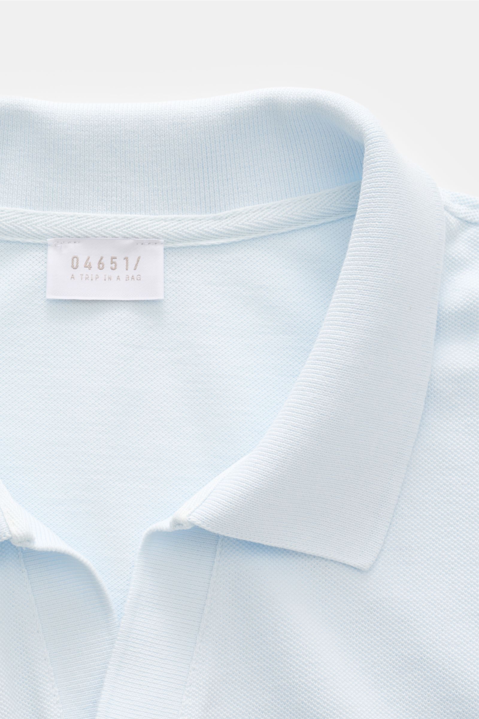 Polnahaufnahme des 04651/ A trip in a bag Poloshirt 'Johnny' pastellblau aus reiner Baumwolle mit offenem Kragen und kleinem Weblabel.