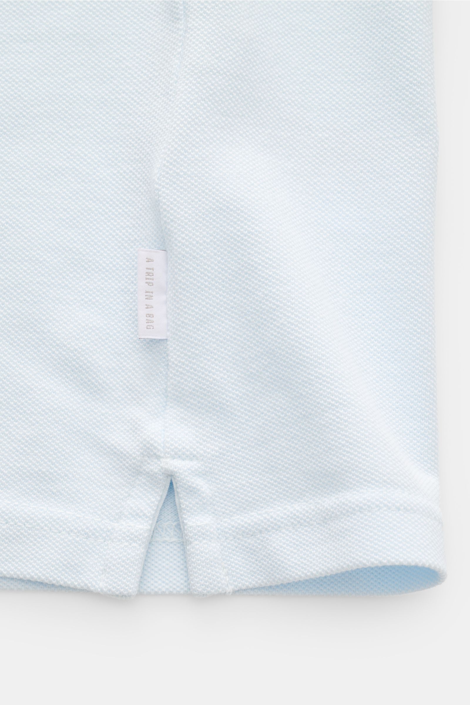 04651/ A trip in a bag Poloshirt 'Johnny' pastellblau, Detailaufnahme Saum mit kurzem Schlitz, Piqué-Baumwolle, Weblabel seitlich.
