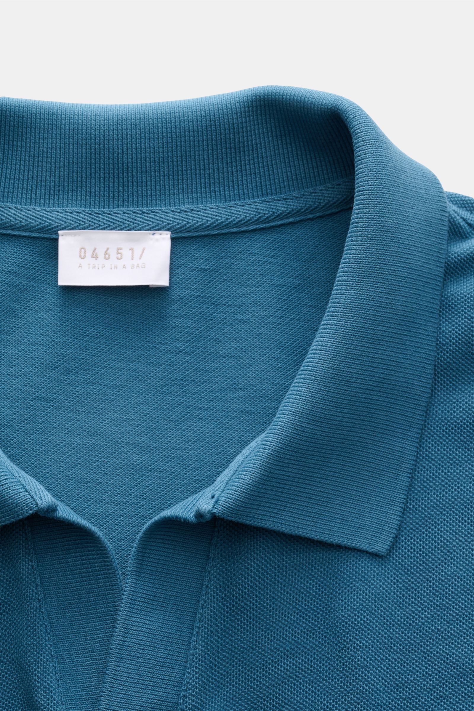 04651/ A trip in a bag Poloshirt 'Johnny' petrol aus reiner Baumwolle, offener Kragen, Regular Fit, Detailansicht Kragen und Label, leichte Piqué-Haptik.