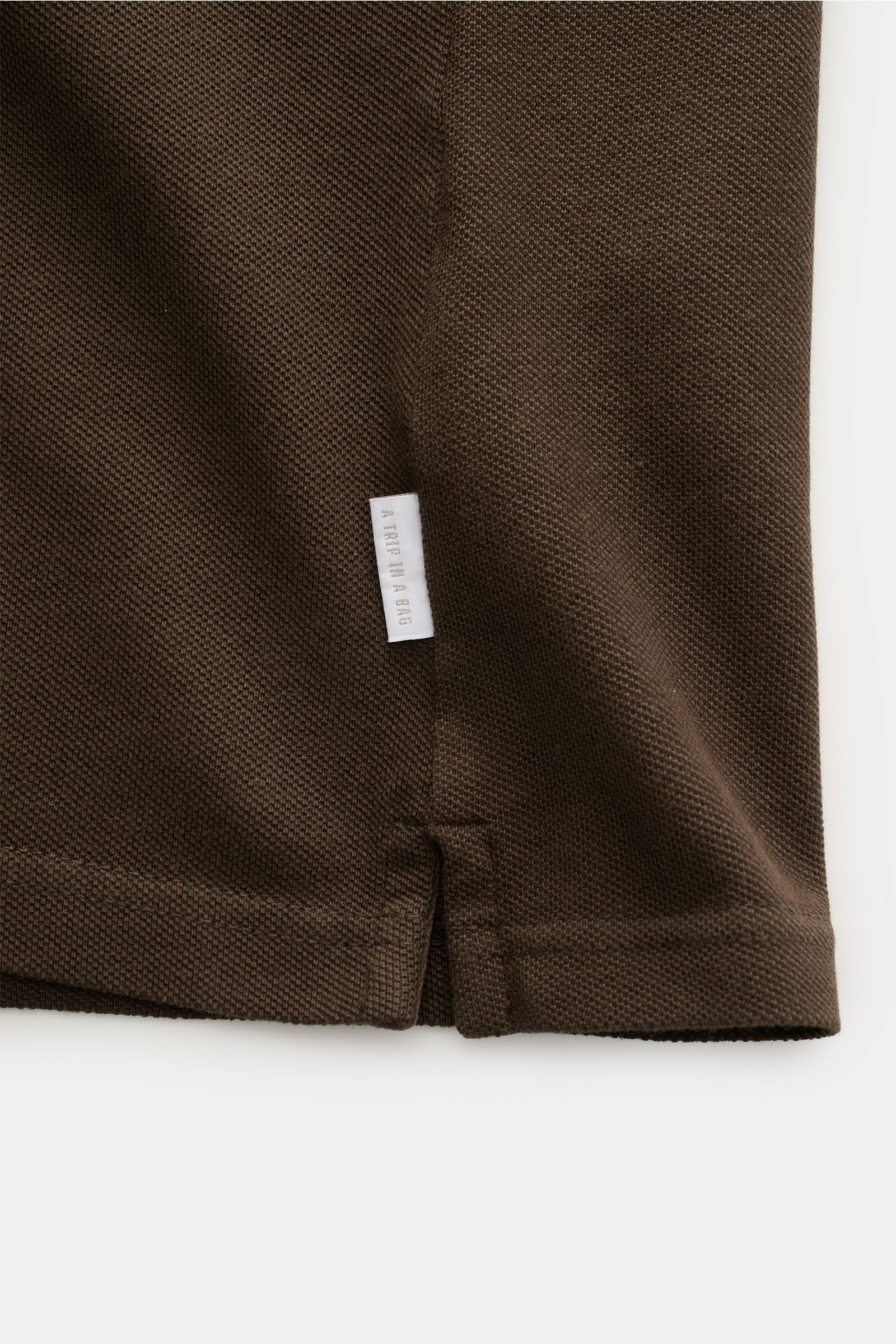 Close-up side detail of the hem and small woven label of the 04651/ A trip in a bag Polo shirt 'Johnny' dark brown in pure piqué cotton.

For relaxed casual looks: 04651/ A TRIP IN A BAG brings a relaxed summer vibe to your wardrobe with this pure cott