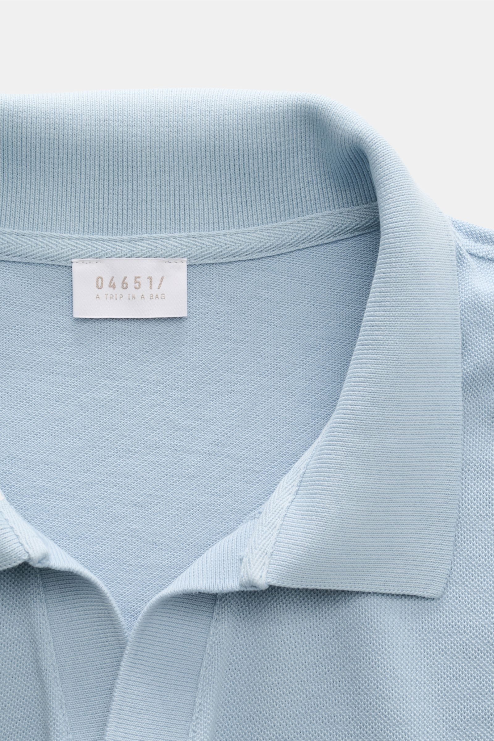Close-up top-down view of the collar and label of the 04651/ A trip in a bag Polo shirt 'Johnny' smoky blue in pure piqué cotton.

For relaxed casual looks: 04651/ A TRIP IN A BAG brings a relaxed summer vibe to your wardrobe with this pure cotton polo