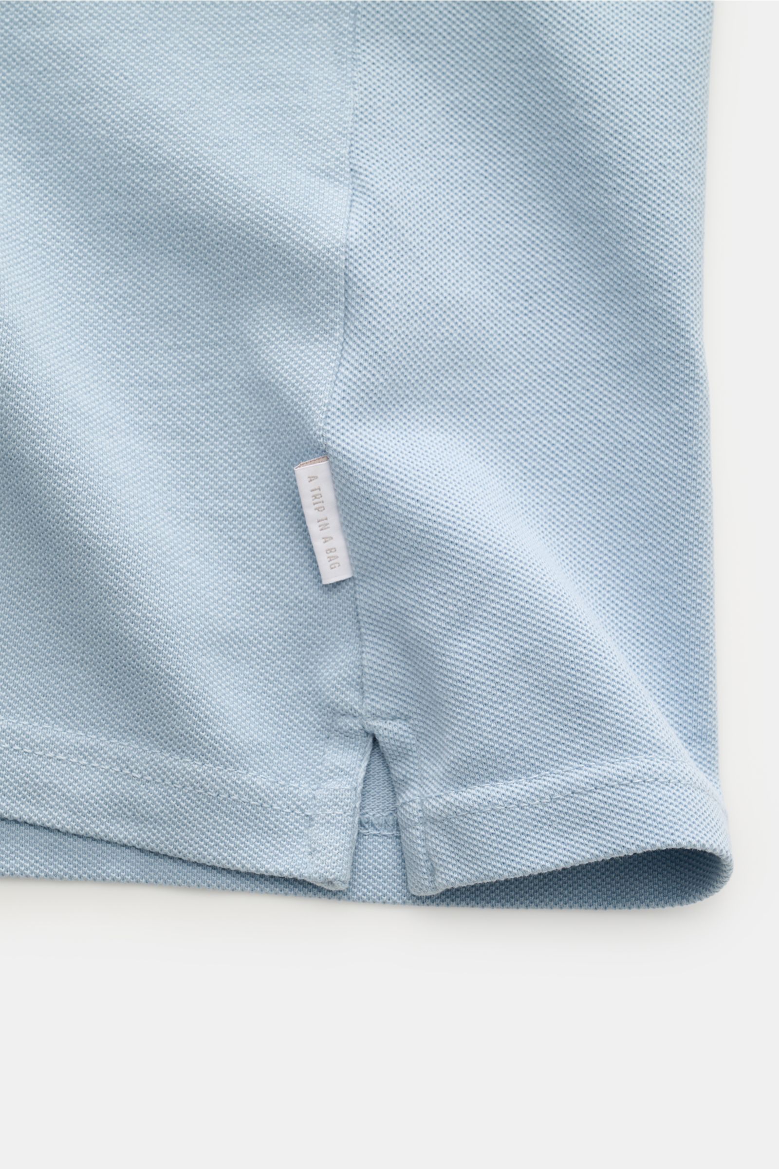 Close-up view of the hem and side seam with woven label of the 04651/ A trip in a bag Polo shirt 'Johnny' smoky blue in pure piqué cotton.

For relaxed casual looks: 04651/ A TRIP IN A BAG brings a relaxed summer vibe to your wardrobe with this pure co