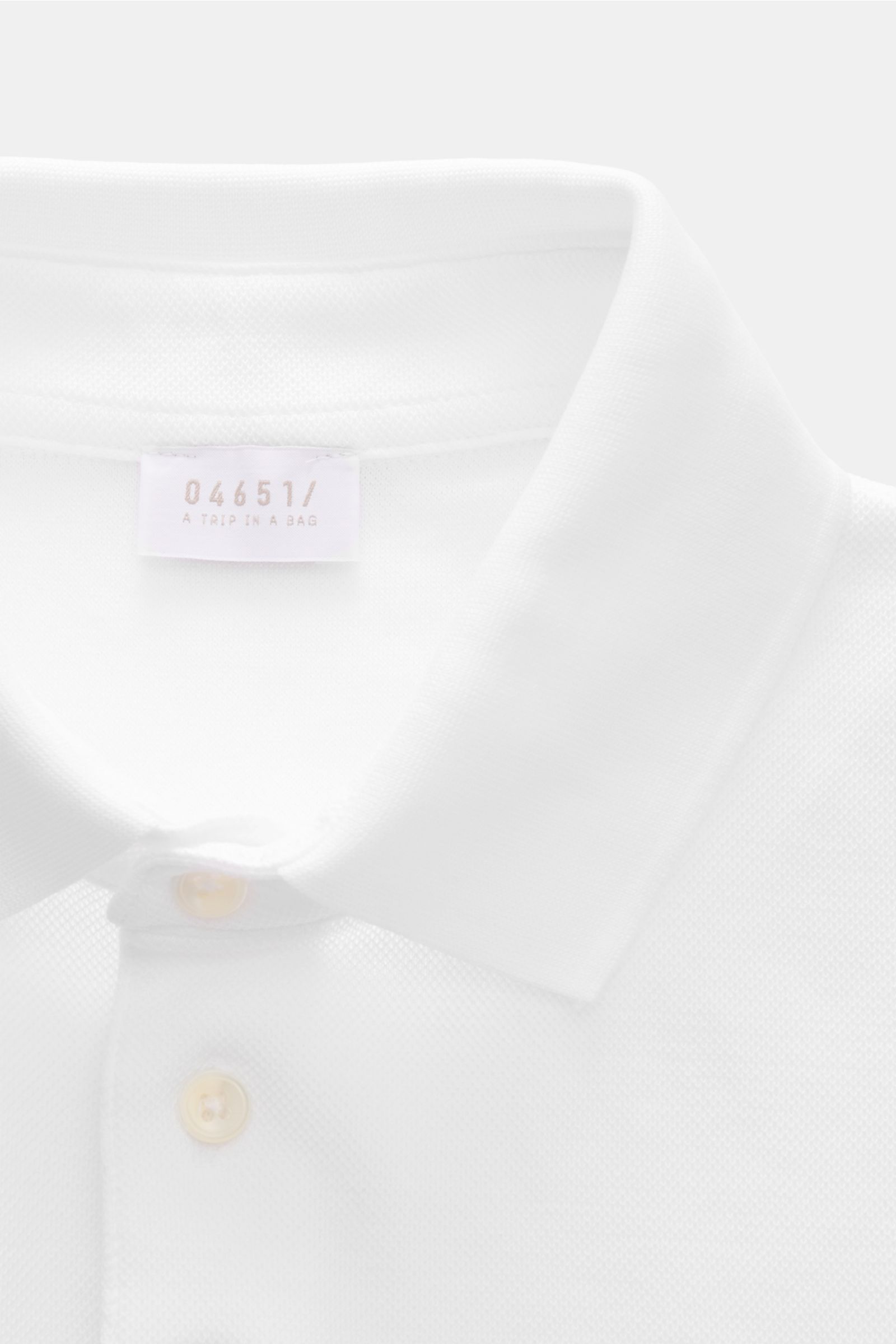 Close-up front view of 04651/ A trip in a bag Poloshirt 'TP' weiß, a white polo shirt made of pure cotton piqué, soft touch, regular fit, with classic collar, smooth button placket, small side seam label, and comfortable ribbed cuffs. Ob im Urlaub oder