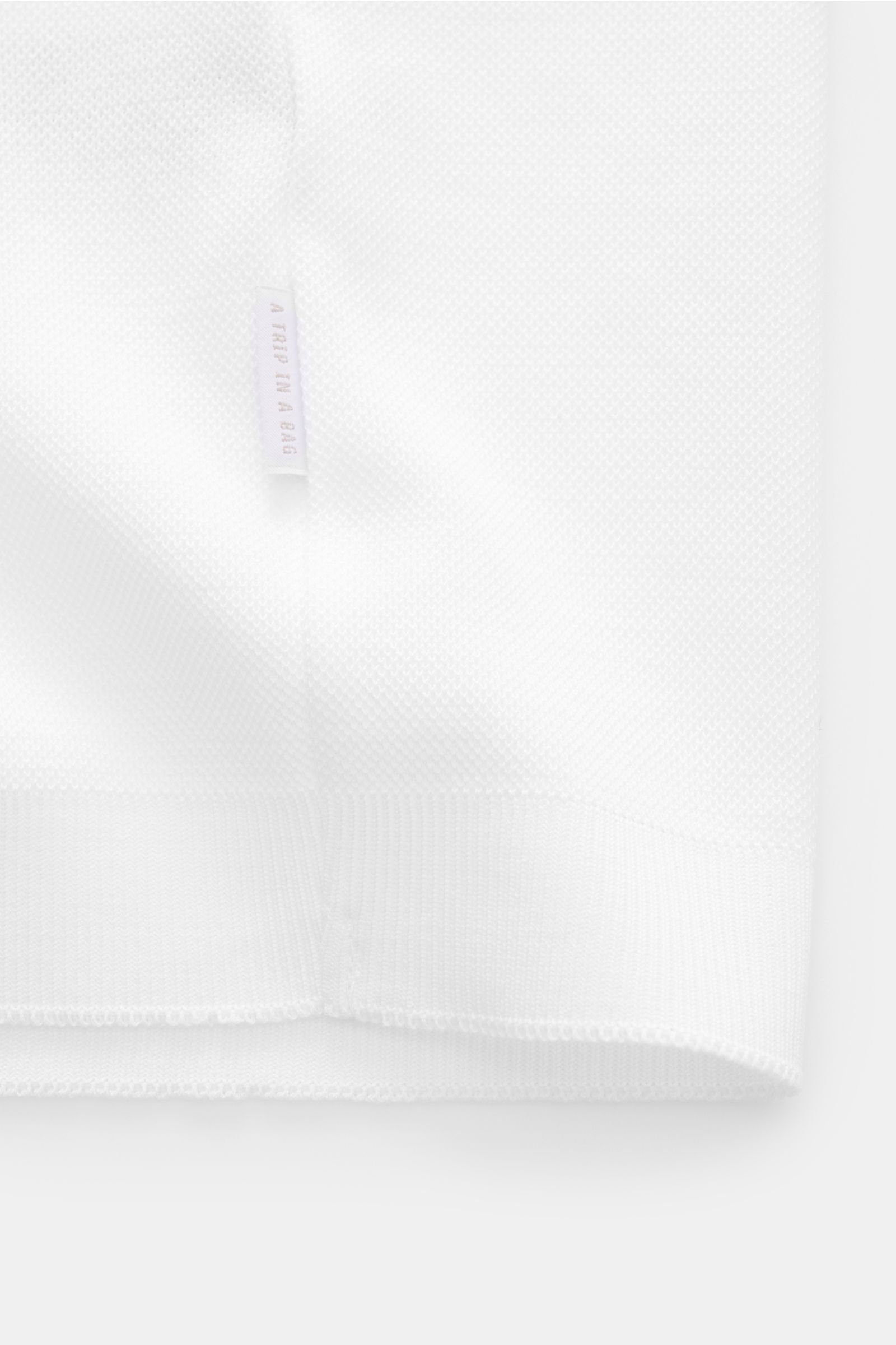 White textured fabric close-up of the lower hem and side seam of the 04651/ A trip in a bag Poloshirt 'TP' weiß, photographed from the front. Ob im Urlaub oder Office: 04651/ A TRIP IN A BAG bringt mit dem Poloshirt aus reiner Baumwolle lässiges Sommer