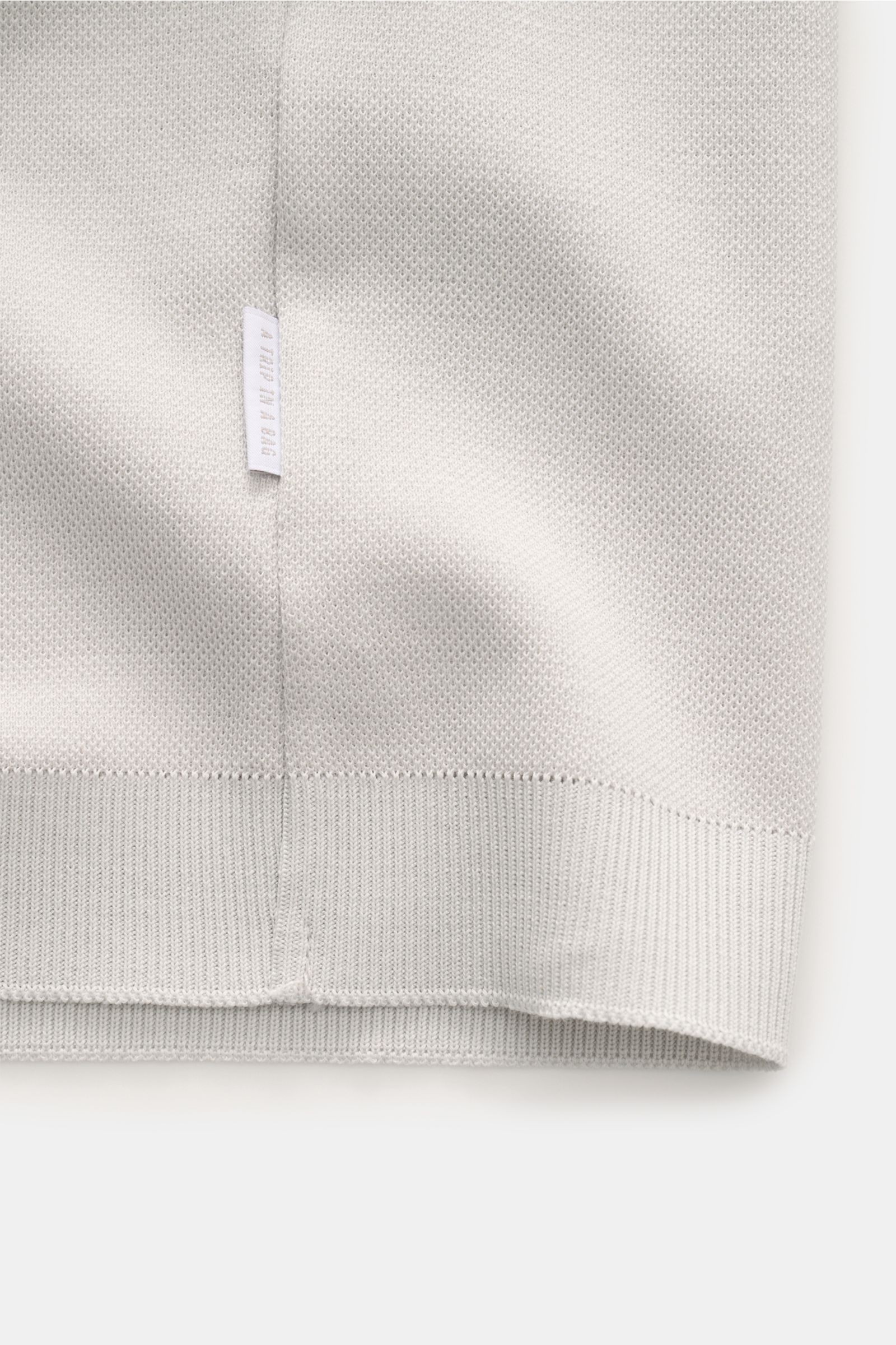 Hellgraues Detailbild des 04651/ A trip in a bag Poloshirt 'TP' hellgrau von unten, zeigt Piqué aus reiner Baumwolle, weichen Griff, komfortable Rippbündchen und kleines Weblabel in der Seitennaht.