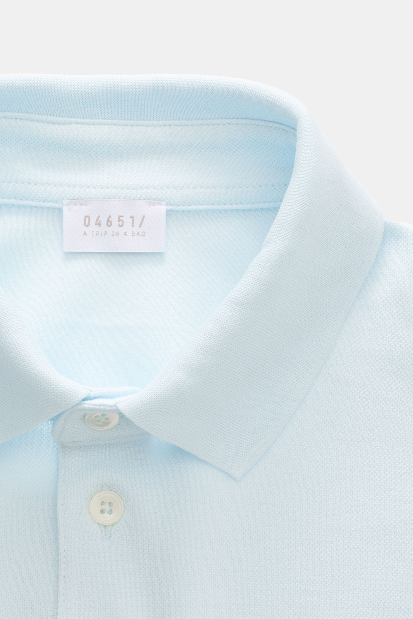 Close-up front view of the 04651/ A trip in a bag Poloshirt 'TP' pastellblau, showing classic collar, smooth button placket, and soft cotton piqué fabric. Ob im Urlaub oder Office: 04651/ A TRIP IN A BAG bringt mit dem Poloshirt aus reiner Baumwolle lä