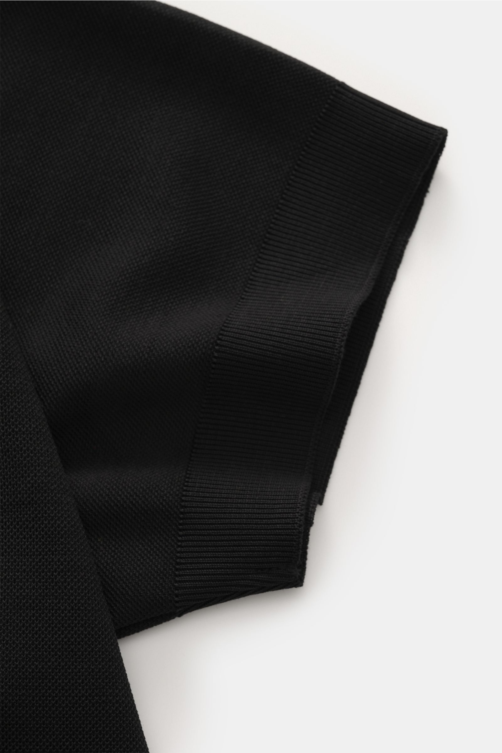 Close-up side view of the sleeve of the 04651/ A trip in a bag Poloshirt 'TP' schwarz, made of pure cotton piqué with a soft feel, regular fit, classic polo collar, smooth button placket, small woven label in side seam, and comfortable ribbed cuffs. Ob