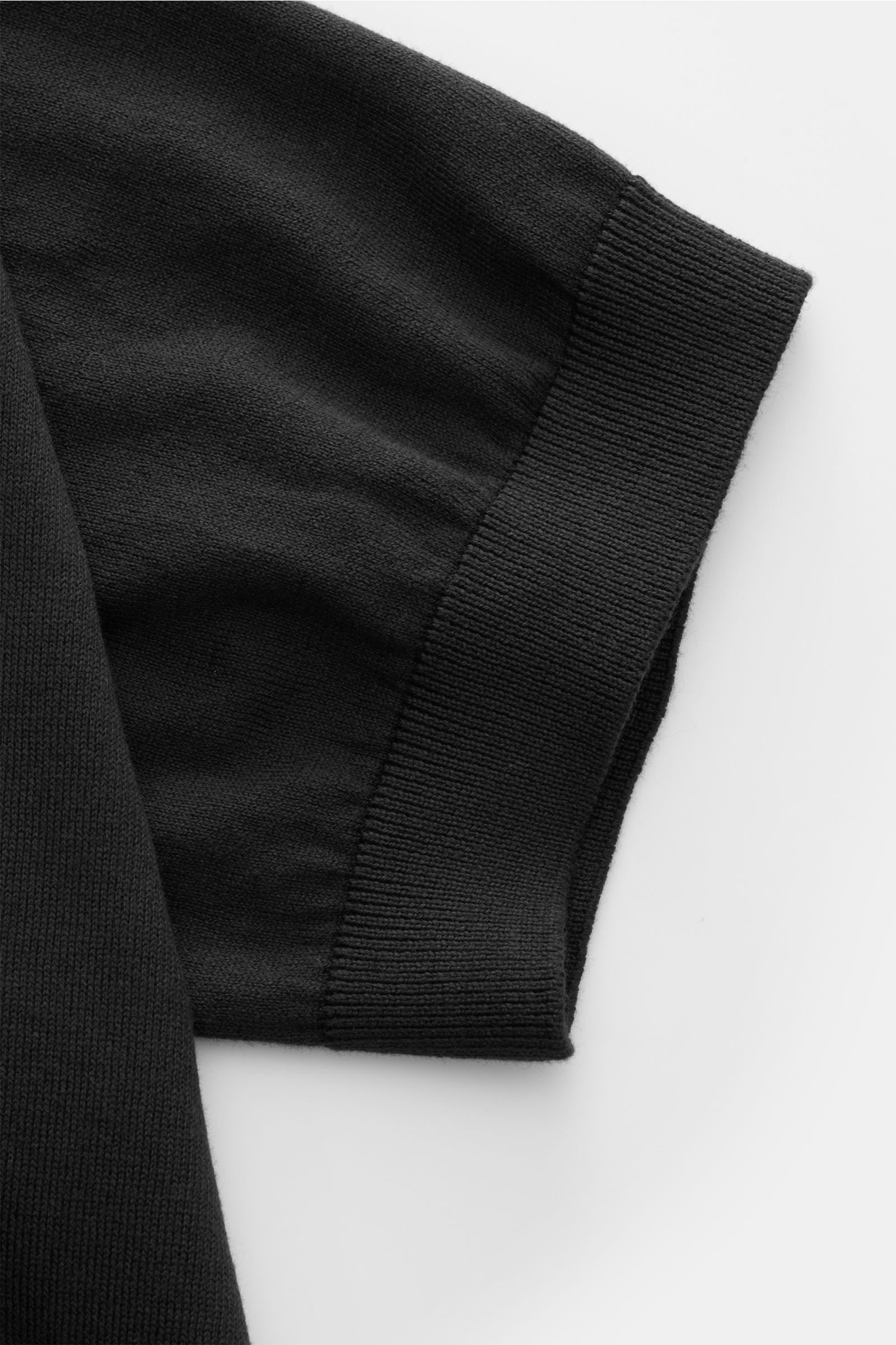 Nahaufnahme des Ärmels von 04651/ A trip in a bag Kurzarm-Strickpolo 'Pima Cotton' schwarz aus feiner Pima-Baumwolle mit feinstrick, weichem Griff, Slim Fit, gestricktem Polokragen, Drei-Knopf-Leiste und flexiblen Rippbündchen, fotografiert von oben.