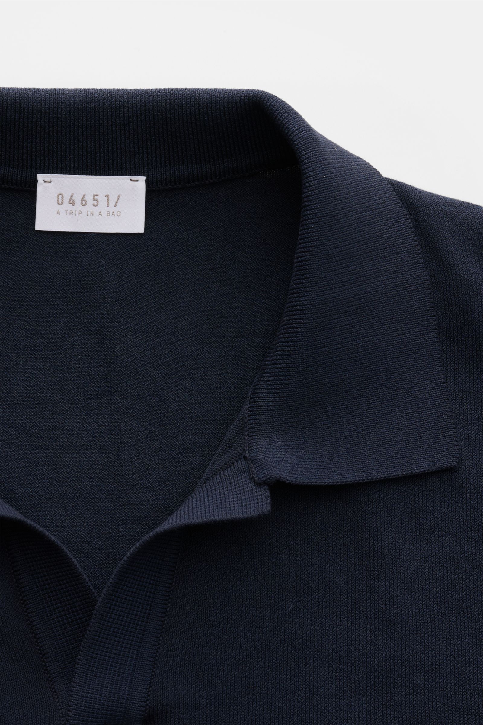 Nahaufnahme von 04651/ A trip in a bag Kurzarm-Strickpolo 'Johnny' navy mit klassischem Polokragen, weichem Griff und feinem Strickbild, fotografiert von oben.