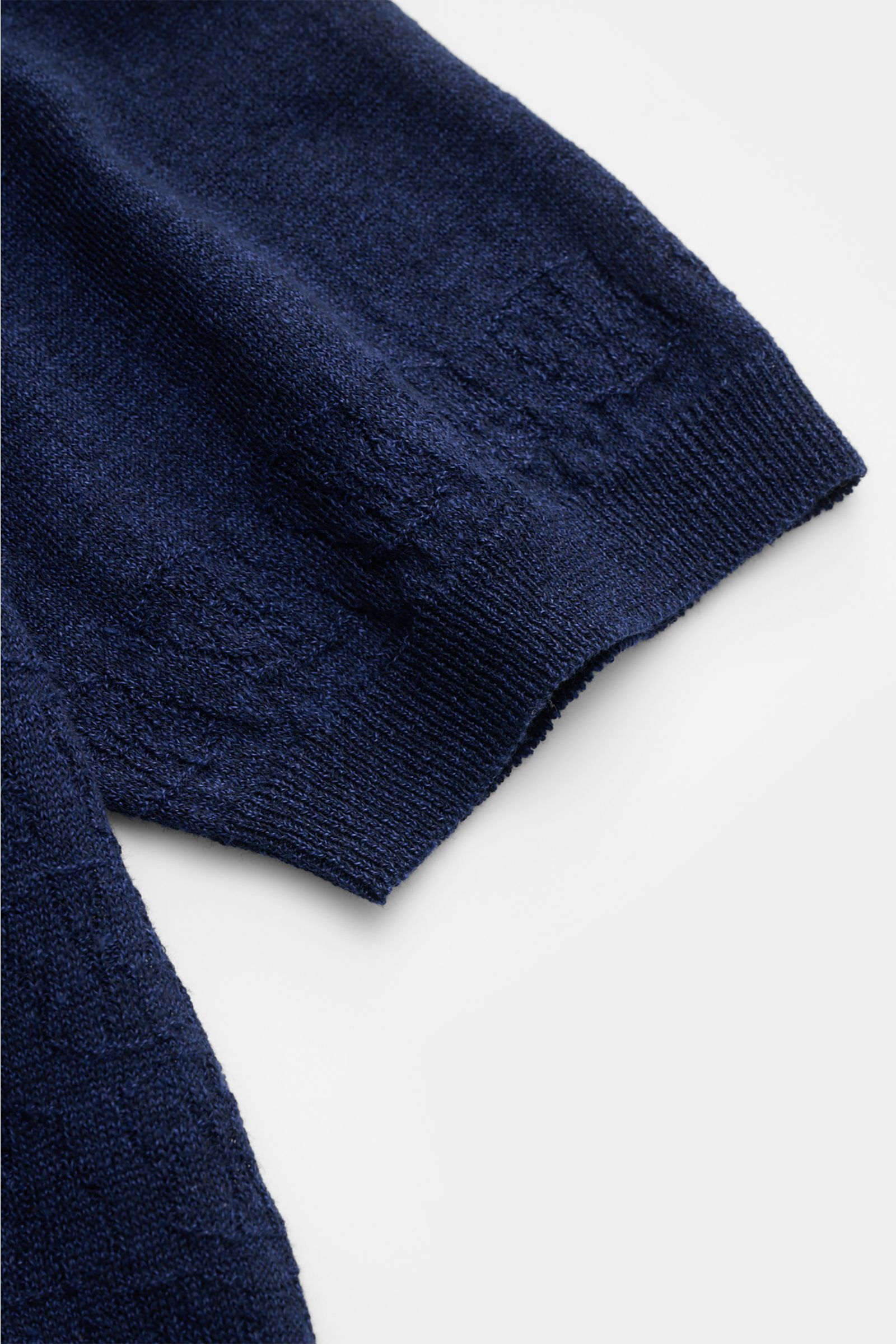 Nahaufnahme des Ärmels und Saums des 04651/ A trip in a bag Kurzarm-Strickpolo 'Hansen' navy, mit feinem Jacquard-Muster, klassischem Polokragen, Oversized Fit, aus Leinen-Baumwoll-Mix mit leicht griffiger Haptik, fotografiert von oben auf weißen Hintergr