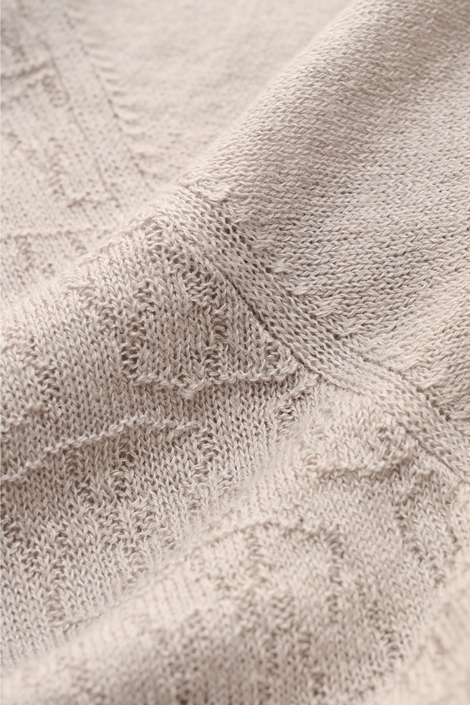 Nahaufnahme des 04651/ A trip in a bag Kurzarm-Strickpolo 'Hansen' hellgrau, sichtbar feiner Jacquard-Strick, Leinen-Baumwoll-Mix, leicht griffig, Oversized Fit, klassischer Polokragen, fotografiert aus schräger Perspektive.