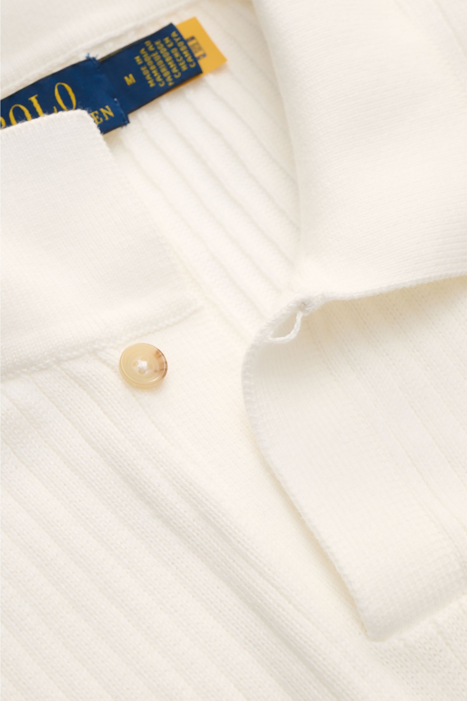 Nahaufnahme aus schräger Perspektive des Polo Ralph Lauren Kurzarm-Strickpolo offwhite mit klassischem Polokragen, Knopf, Rippstrick und weichem Griff.