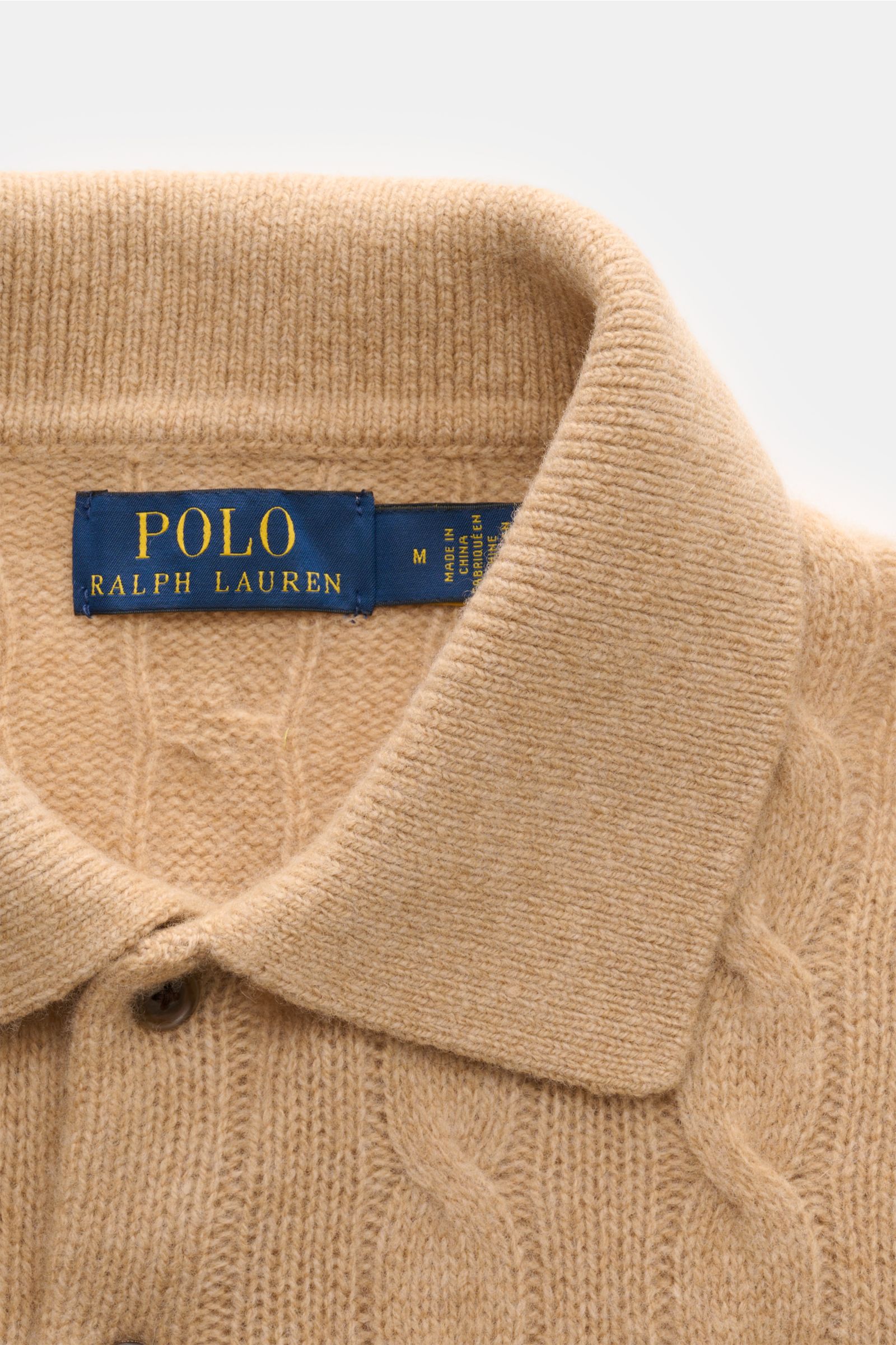 Close-up image from above of the collar and upper chest of the Polo Ralph Lauren Strickpolo grau meliert, showcasing its soft wool and cashmere mix, fine cable knit, slim fit, knitted polo collar, two-button placket, and elastic rib cuffs. Mit diesem e