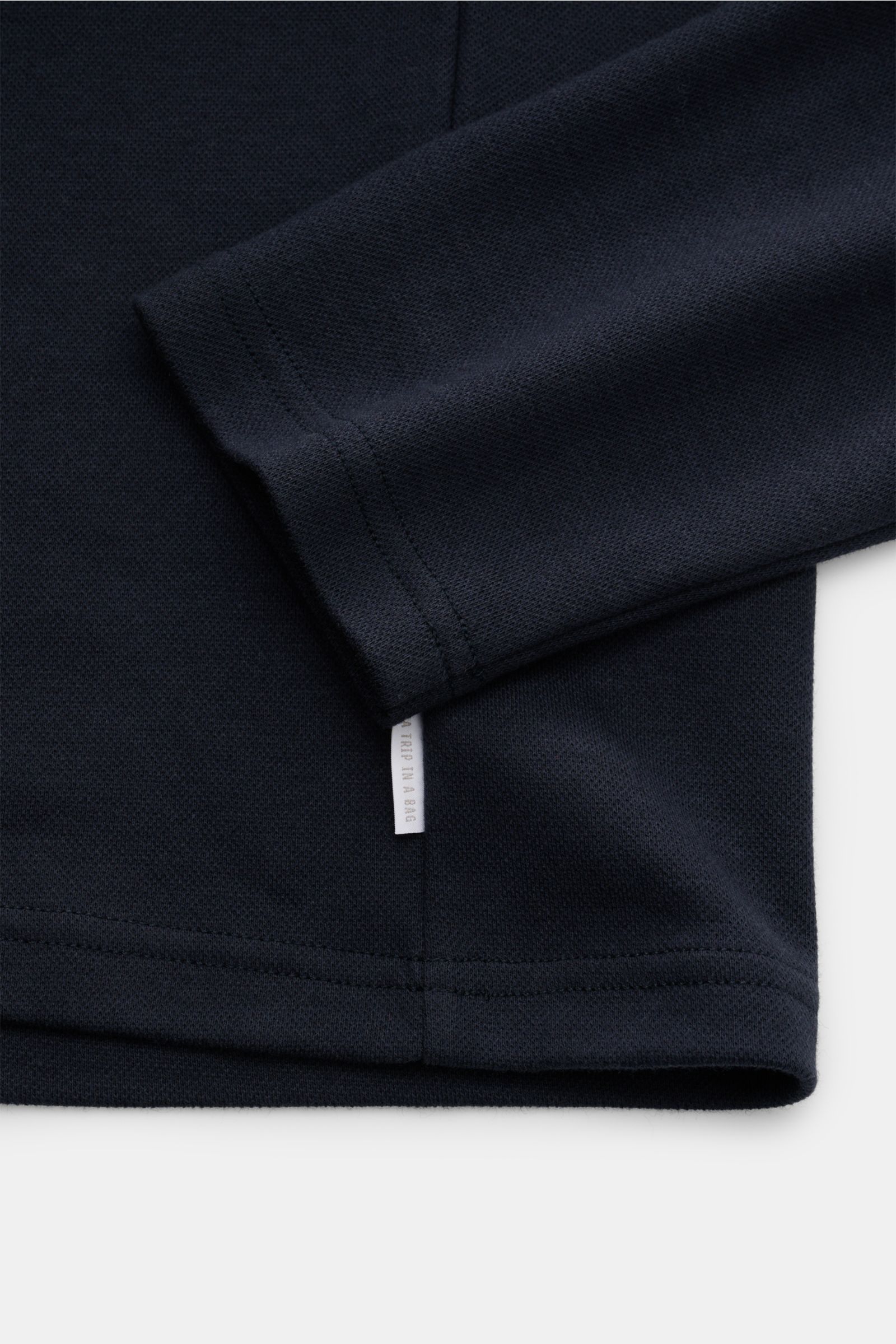 Close-up front-side view of the sleeve and hem of the 04651/ A trip in a bag Longsleeve-Poloshirt dark navy in soft cotton-cashmere piqué jersey with a small white woven label at the side seam.

Dieses Longsleeve-Poloshirt von 04651/ A TRIP IN A BAG au
