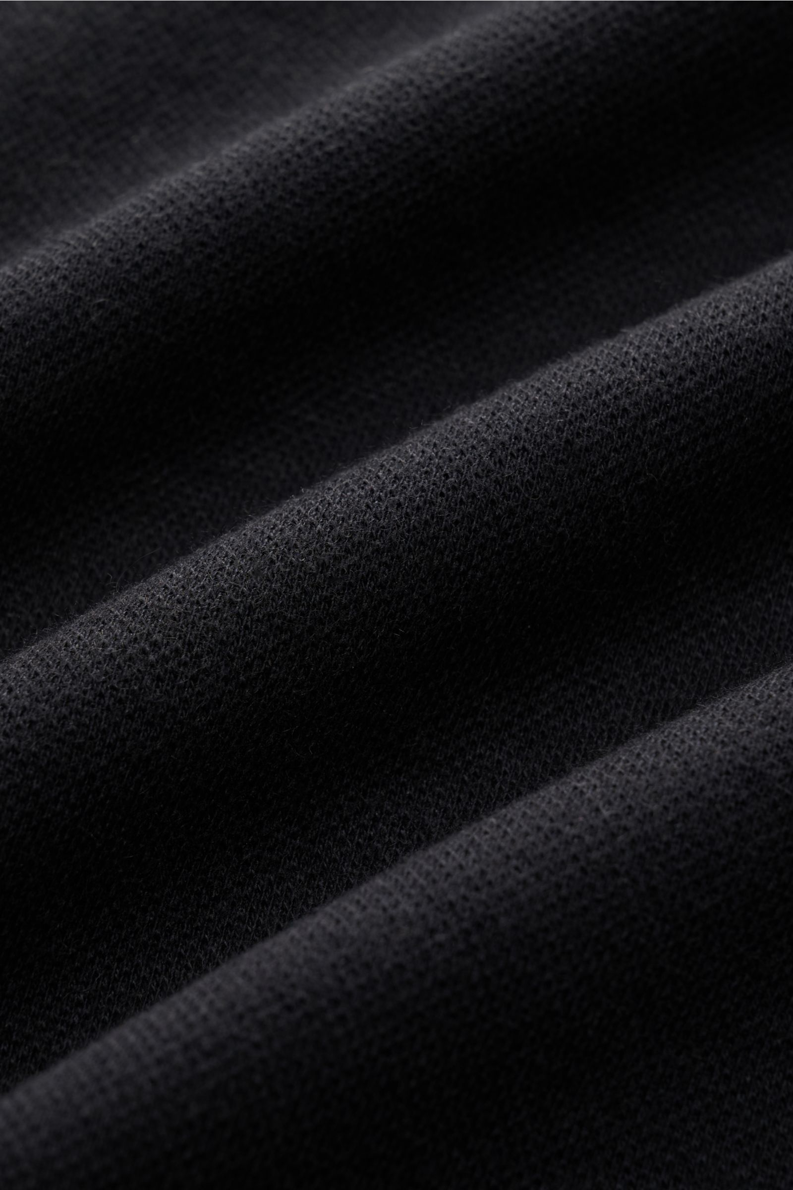 Schwarzer Stoff in Nahaufnahme, Detailaufnahme der weichen Piqué-Jersey-Struktur des 04651/ A trip in a bag Longsleeve-Poloshirt schwarz aus Baumwoll-Cashmere-Mix.