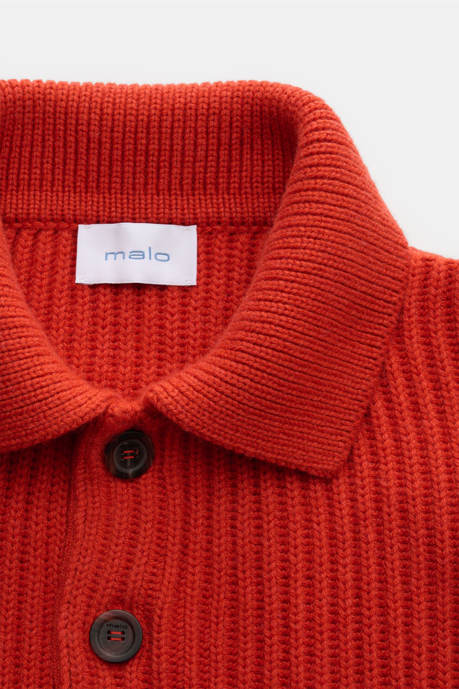 Nahaufnahme des kragenbereichs vom Malo Cashmere Strickpolo orange in grobem Patent-Strickmuster, Oversized Fit mit drei Knöpfen, elastischen Rippbündchen, aus reinem, weichem Cashmere, fotografiert von oben.