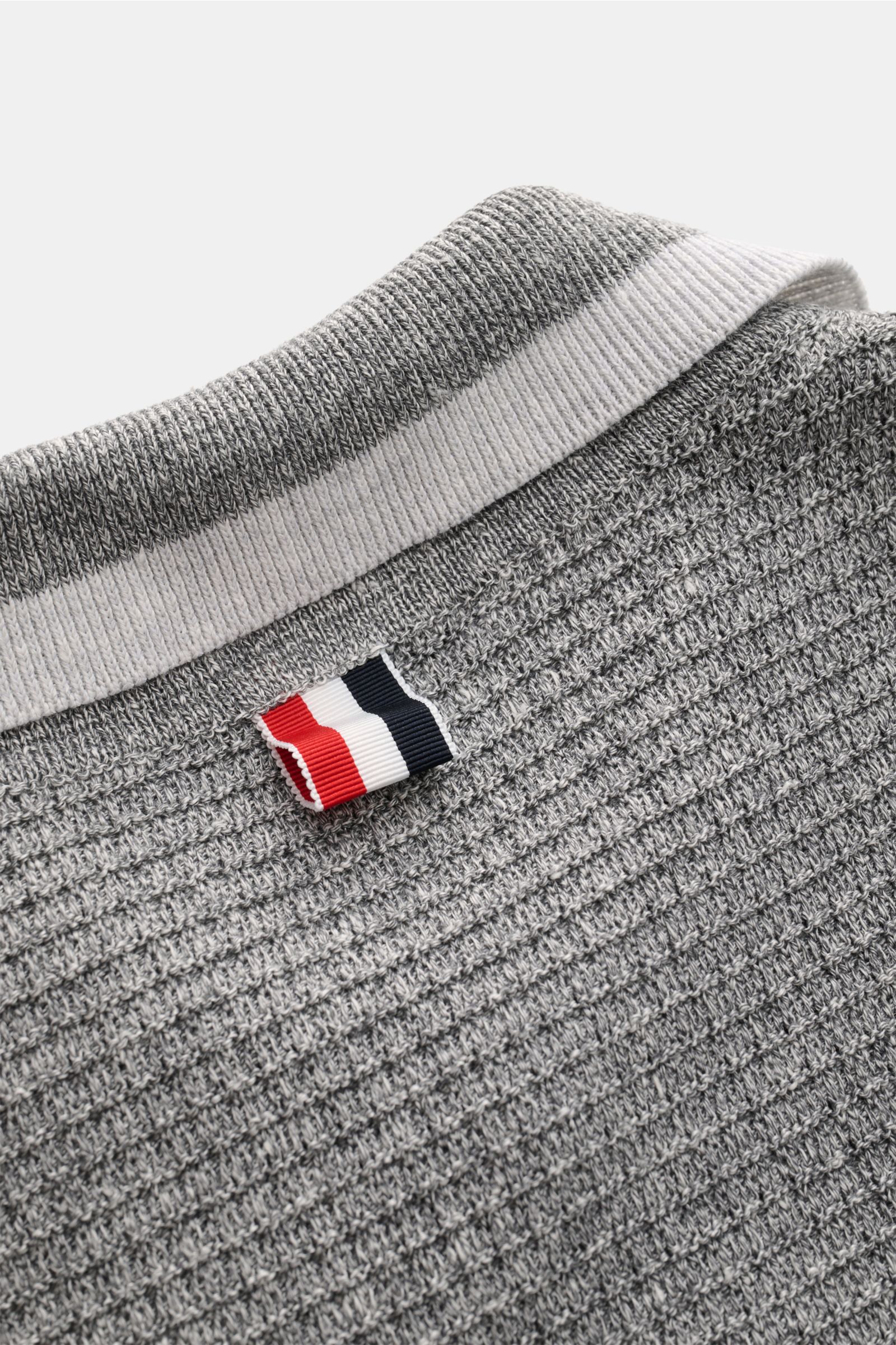 Close-up rear top view of the Thom Browne Strickpolo grau meliert showing the grey melange structure knit, ribbed polo collar with white stripe, and signature tricolor fabric tag. Vielseitiger Style-Favorit: Das Strickpolo vom U.S.-Designer THOM BROWNE ko